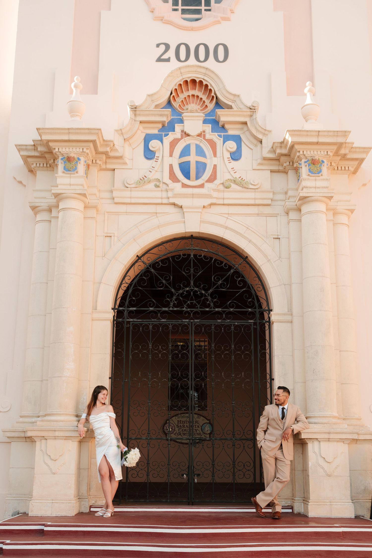 Bride and groom posing at ornate church entrance with arched door and decorative facade marked 2000.