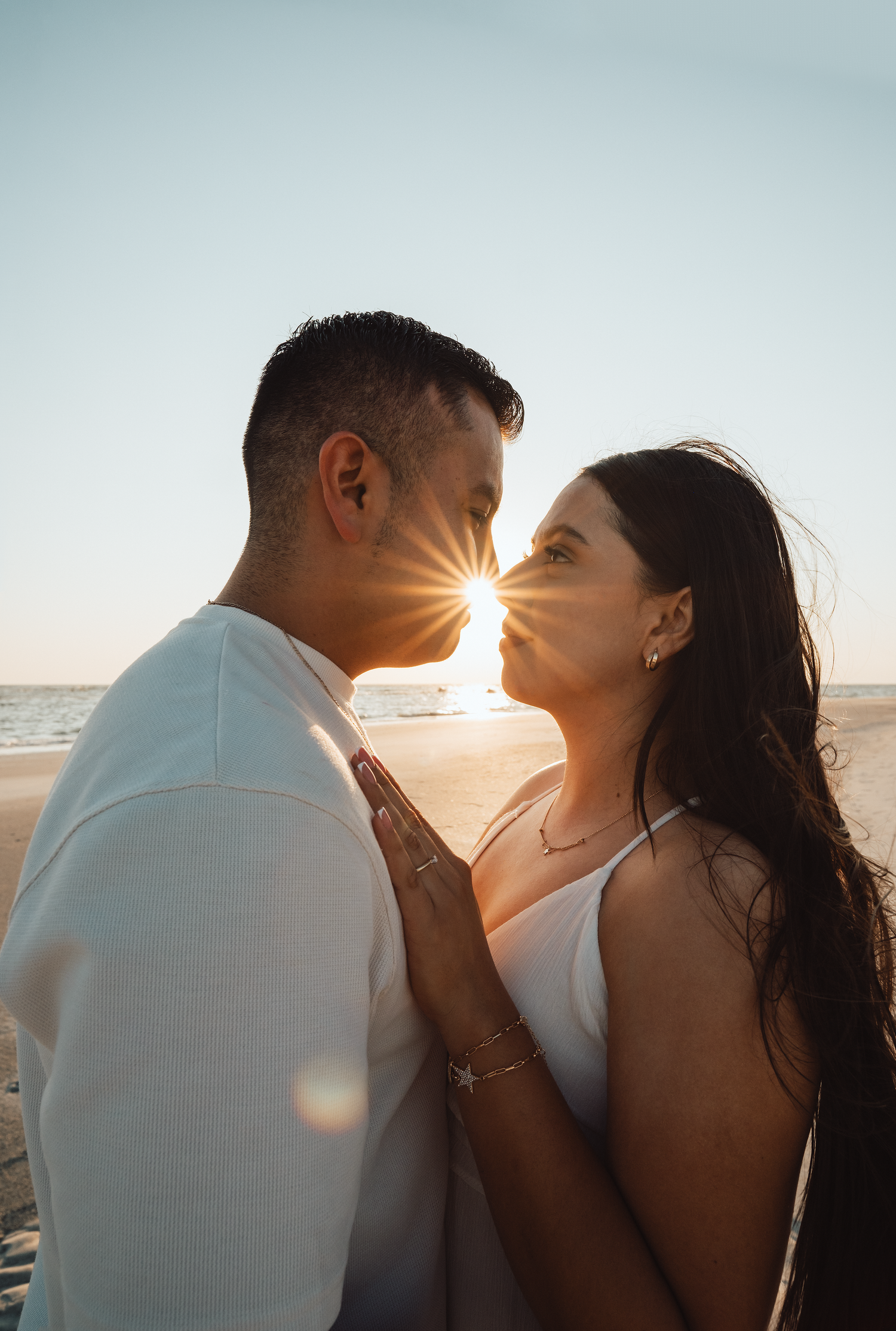 Couple sharing a romantic moment at sunset on the beach, with golden sun flare between them.