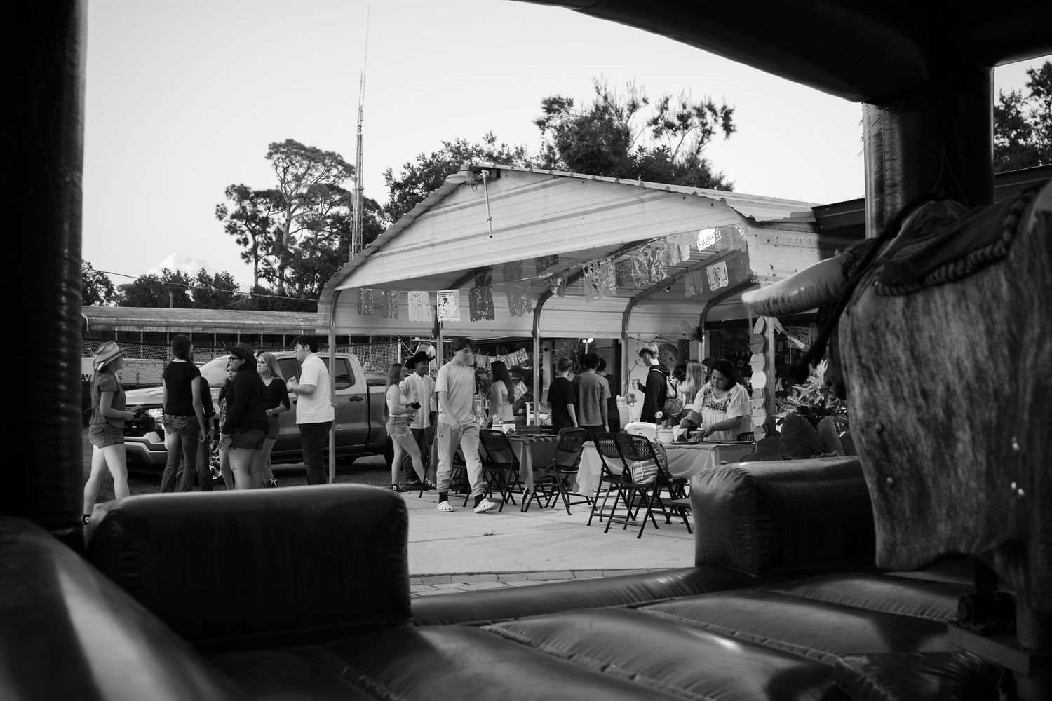 Black and white photo of people gathered outdoors near a building with an awning at a casual event.