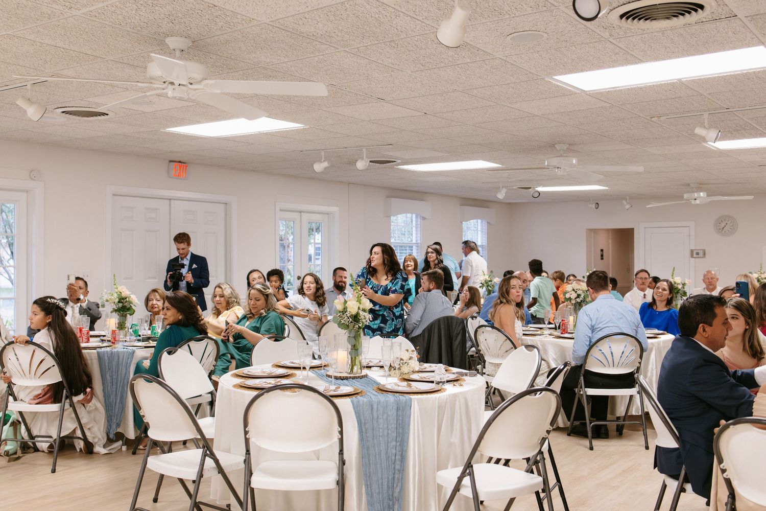 Wedding reception guests seated at round tables in bright decorated banquet hall.