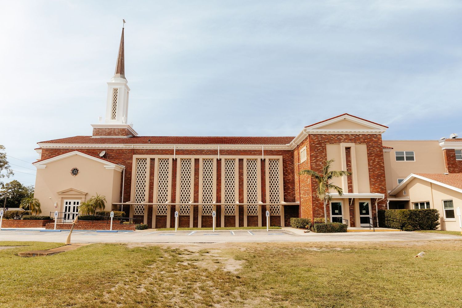 Brick church building with white steeple and decorative facade under partly cloudy sky in Florida.