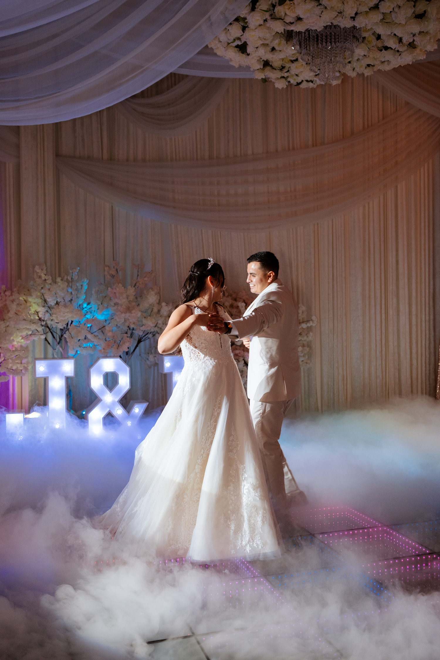 Bride and groom share first dance on foggy LED dance floor with illuminated T&A monogram.