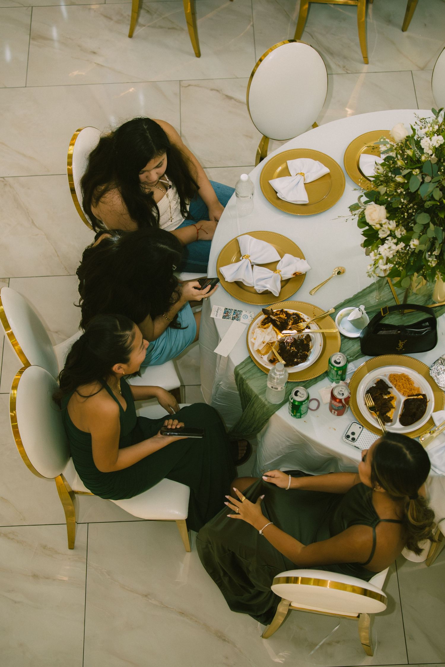 Aerial view of four women dining at an elegant round table with gold chargers and floral centerpiece.