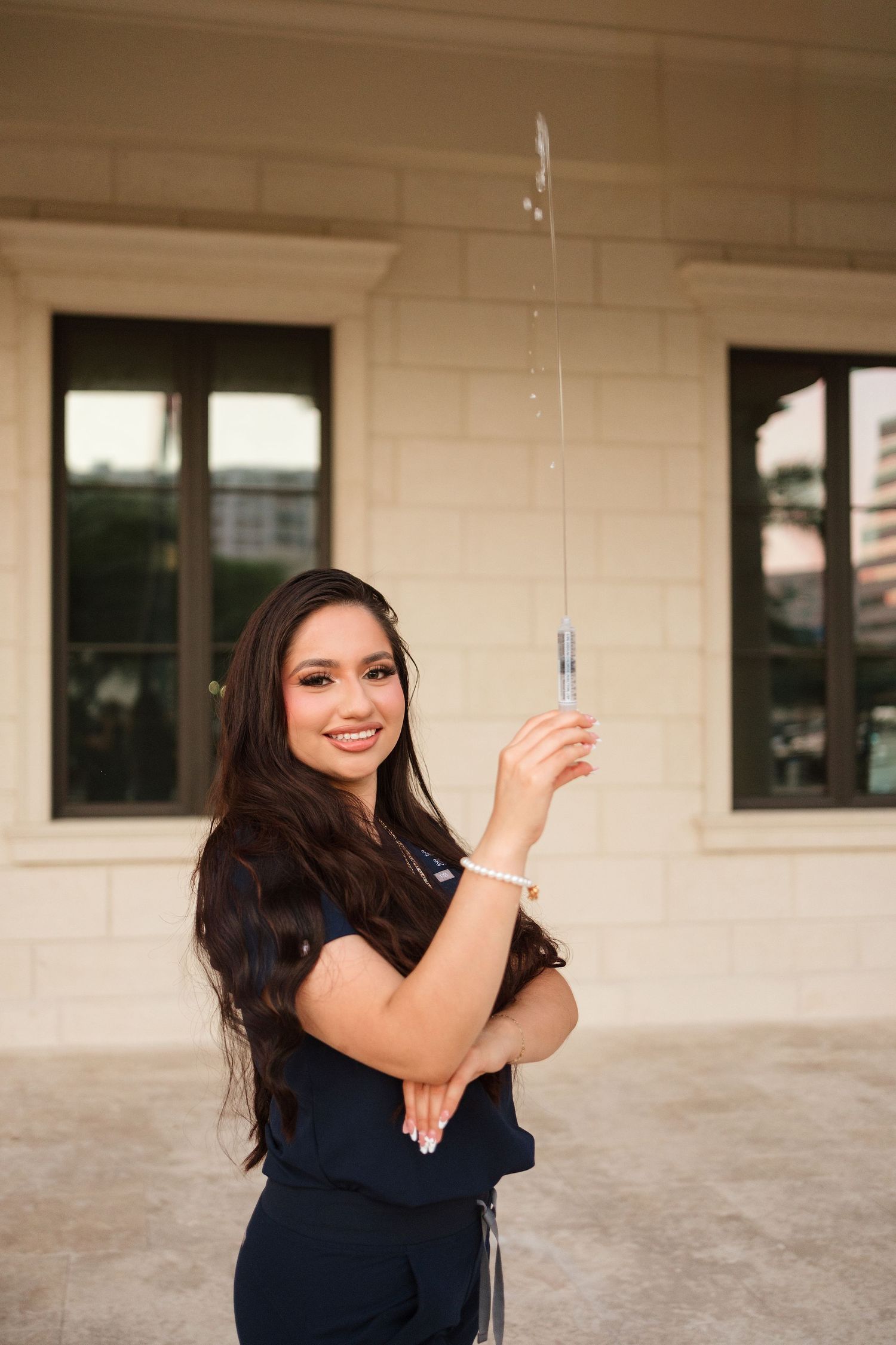 Smiling young woman in navy outfit holds a sparkler outdoors near a beige building.