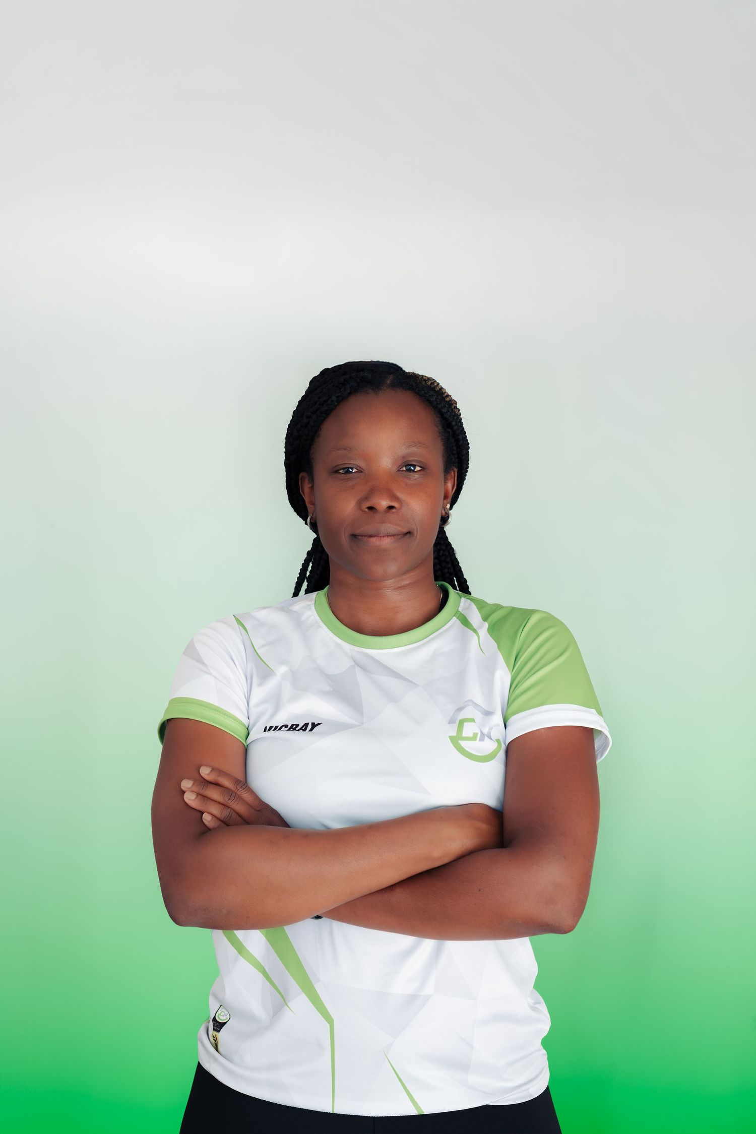 Woman in white and green sports jersey stands confidently with arms crossed against a gradient background.