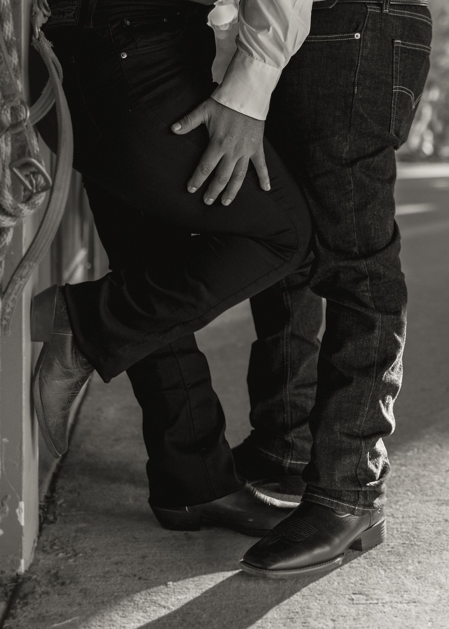 Black and white photo of two people in jeans and cowboy boots standing close together in an intimate pose.