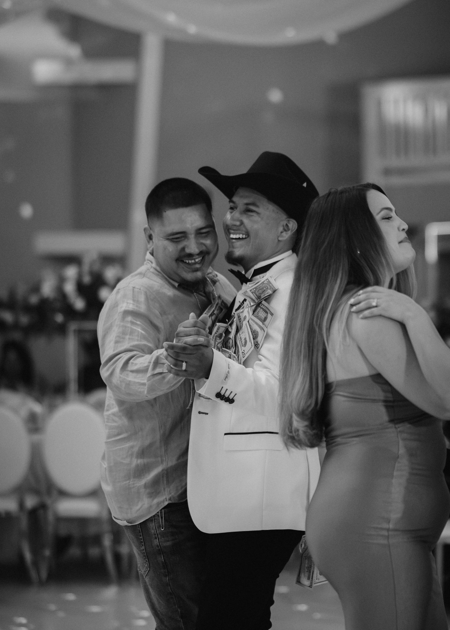 Black and white photo of three people laughing and dancing together at a wedding reception.