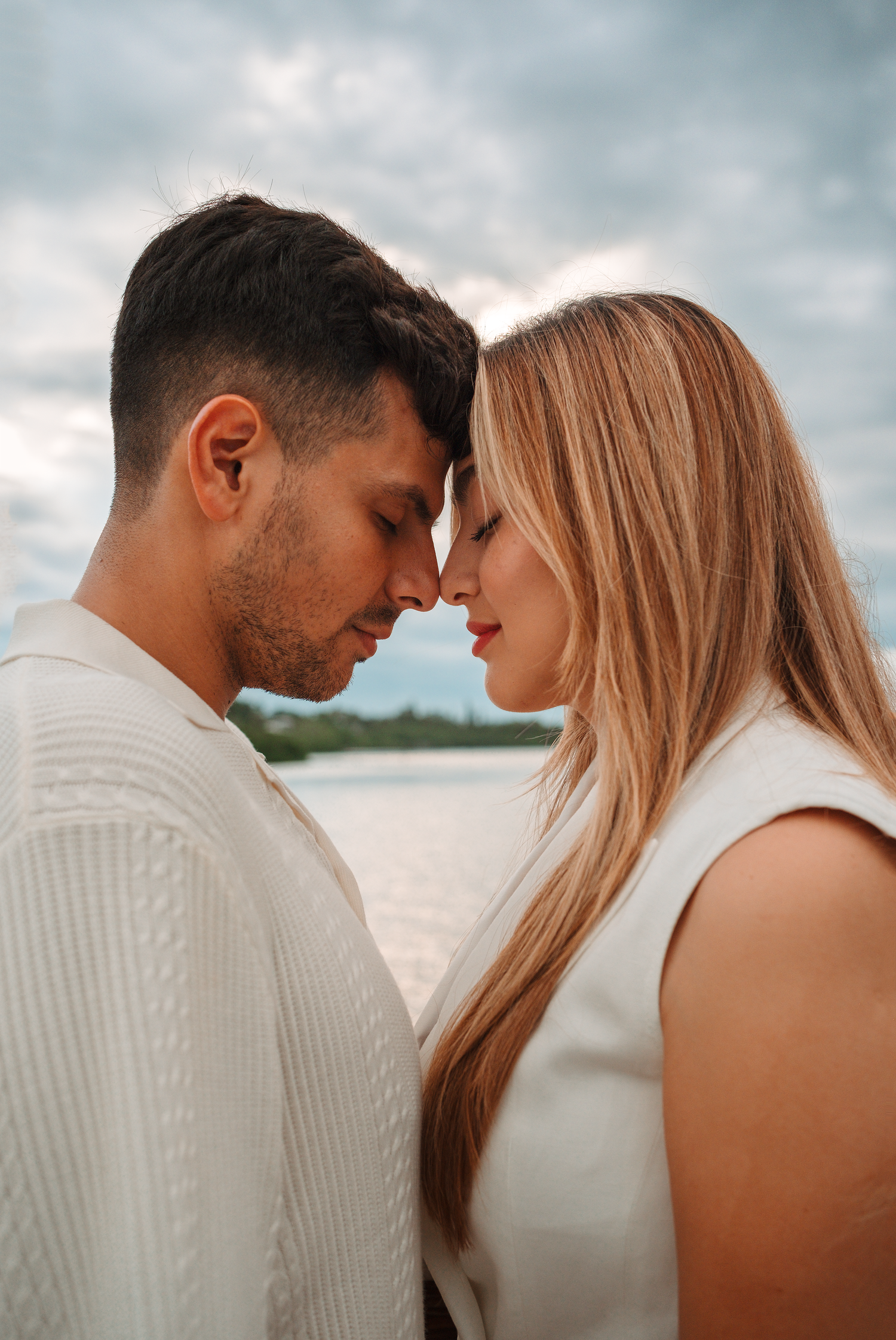 Intimate romantic moment captured against cloudy coastal backdrop.