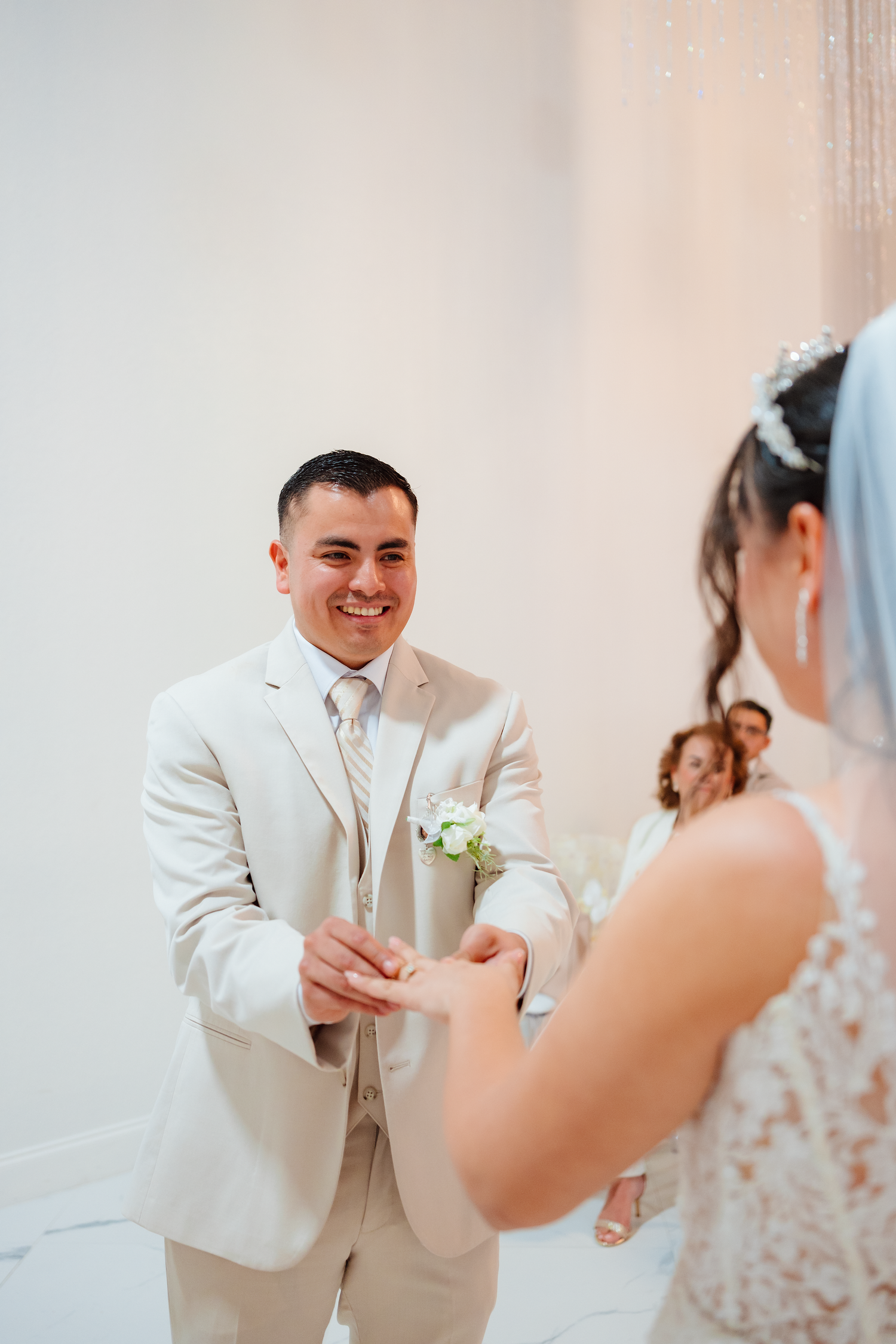 Smiling groom in ivory suit placing wedding ring on brides hand during romantic ceremony.