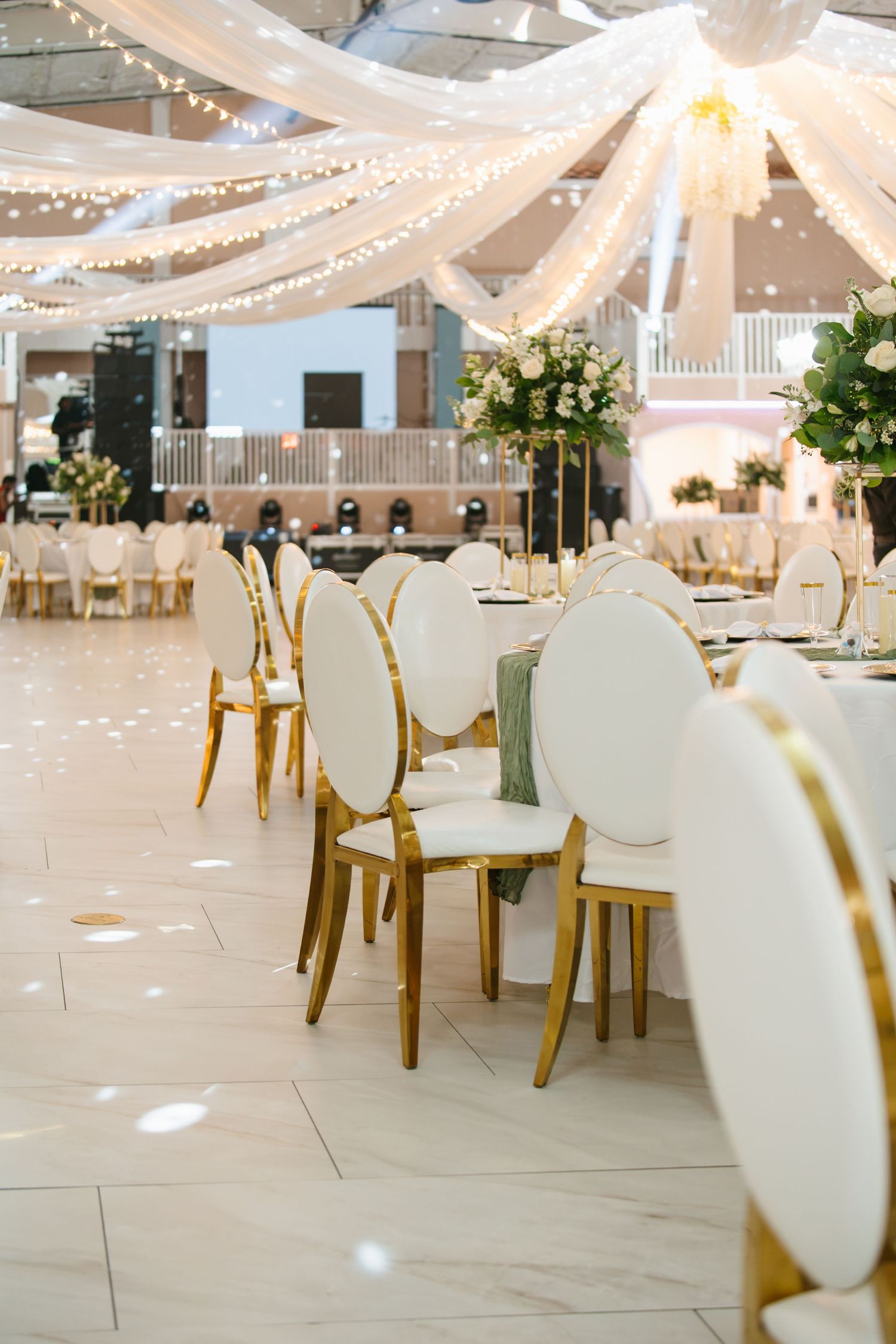 Elegant wedding reception hall with gold chairs, white draping, and string lights.