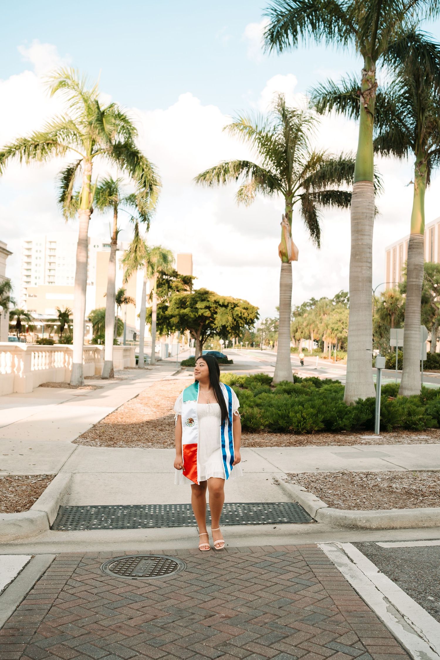 A woman in a colorful outfit stands on a palm tree-lined street in a sunny Florida coastal town.