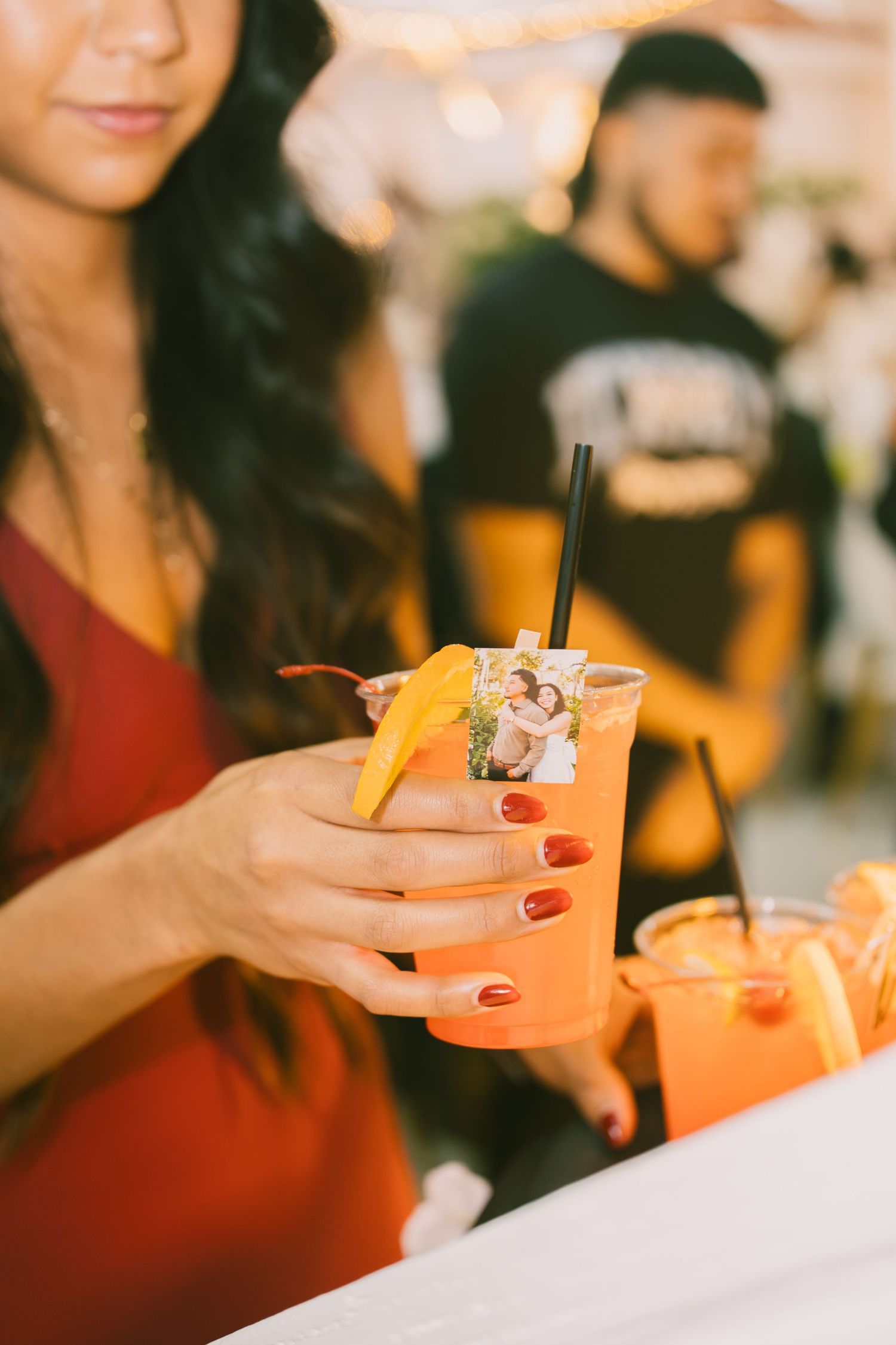Woman in red dress holding an orange cocktail garnished with mango slice and a photo charm.