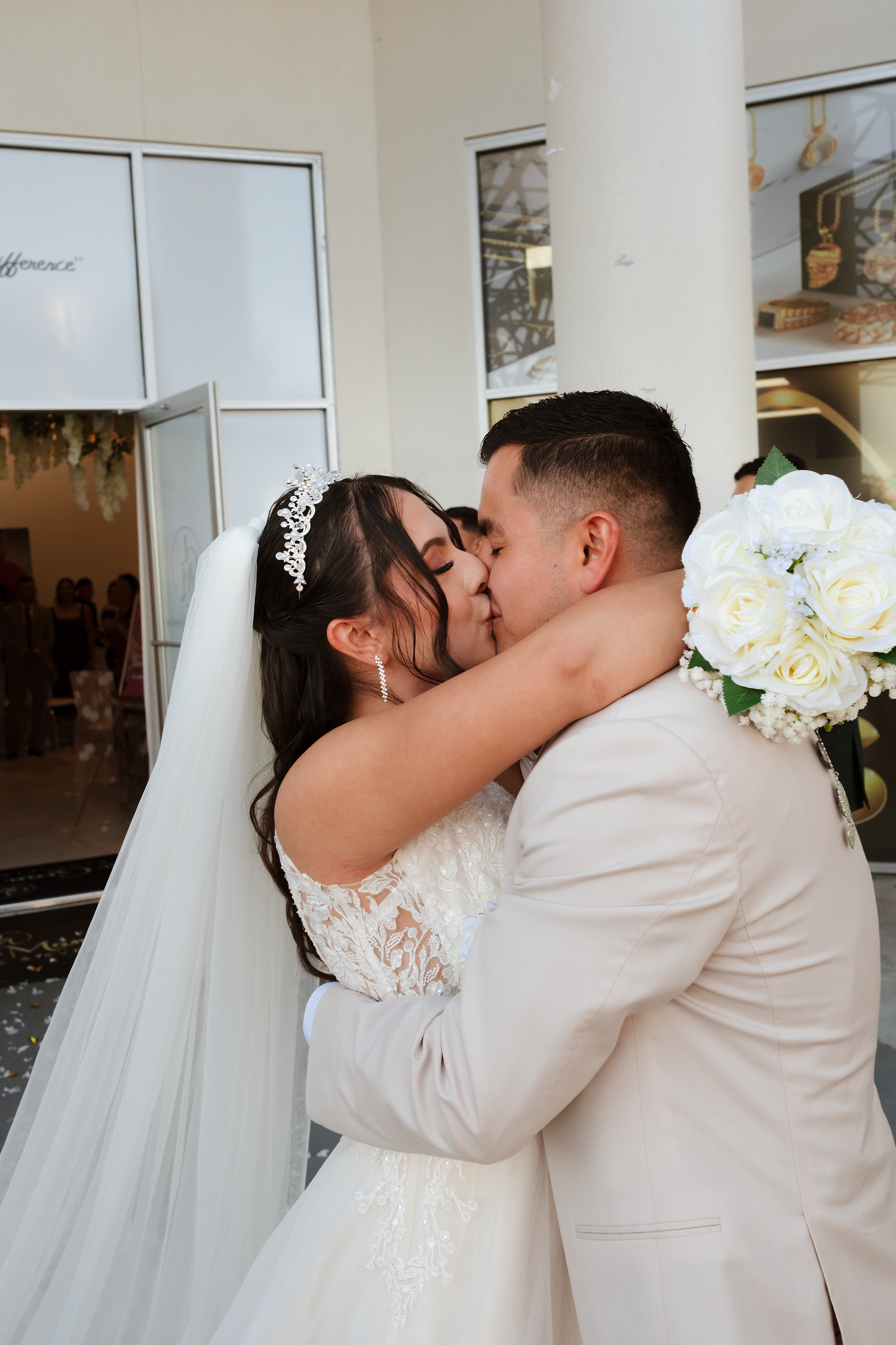 Bride and groom share their first kiss outside wedding venue, bride wearing lace gown and tiara veil.