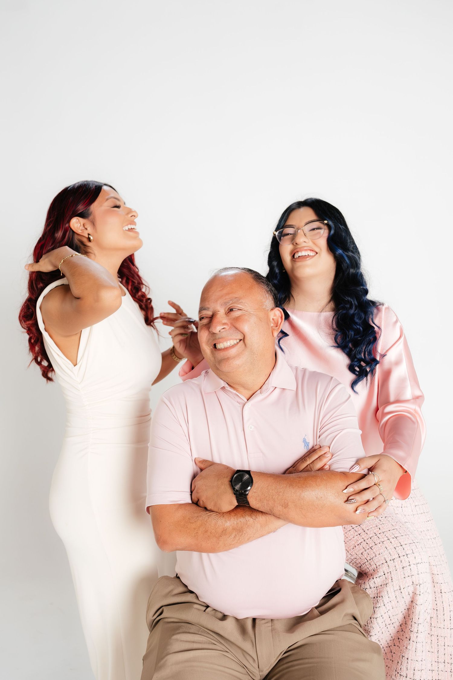 A smiling man with crossed arms poses with two young women with colorful hair against a white background.