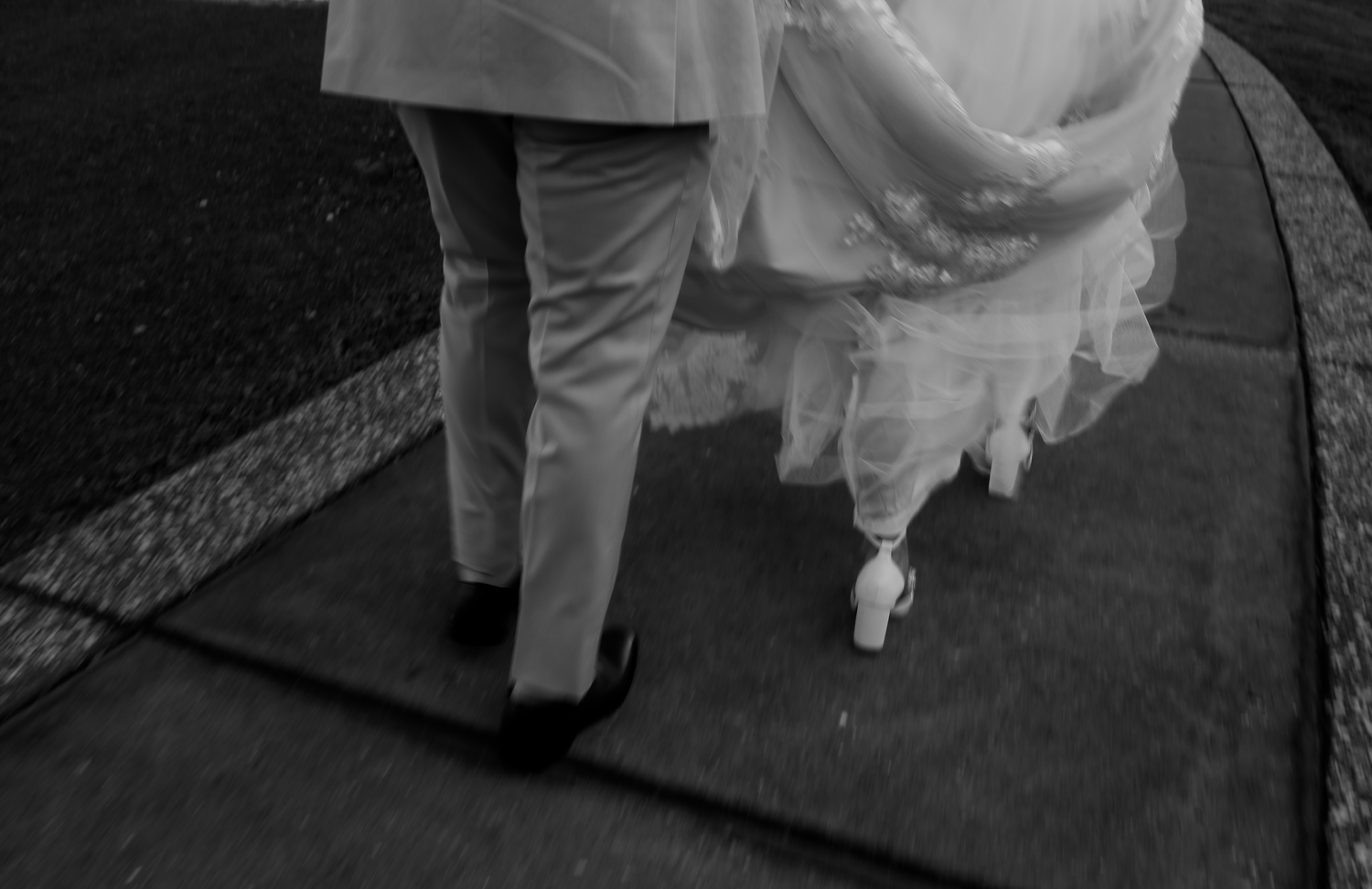 Black and white detail shot of formal attire and flowing dress while walking.