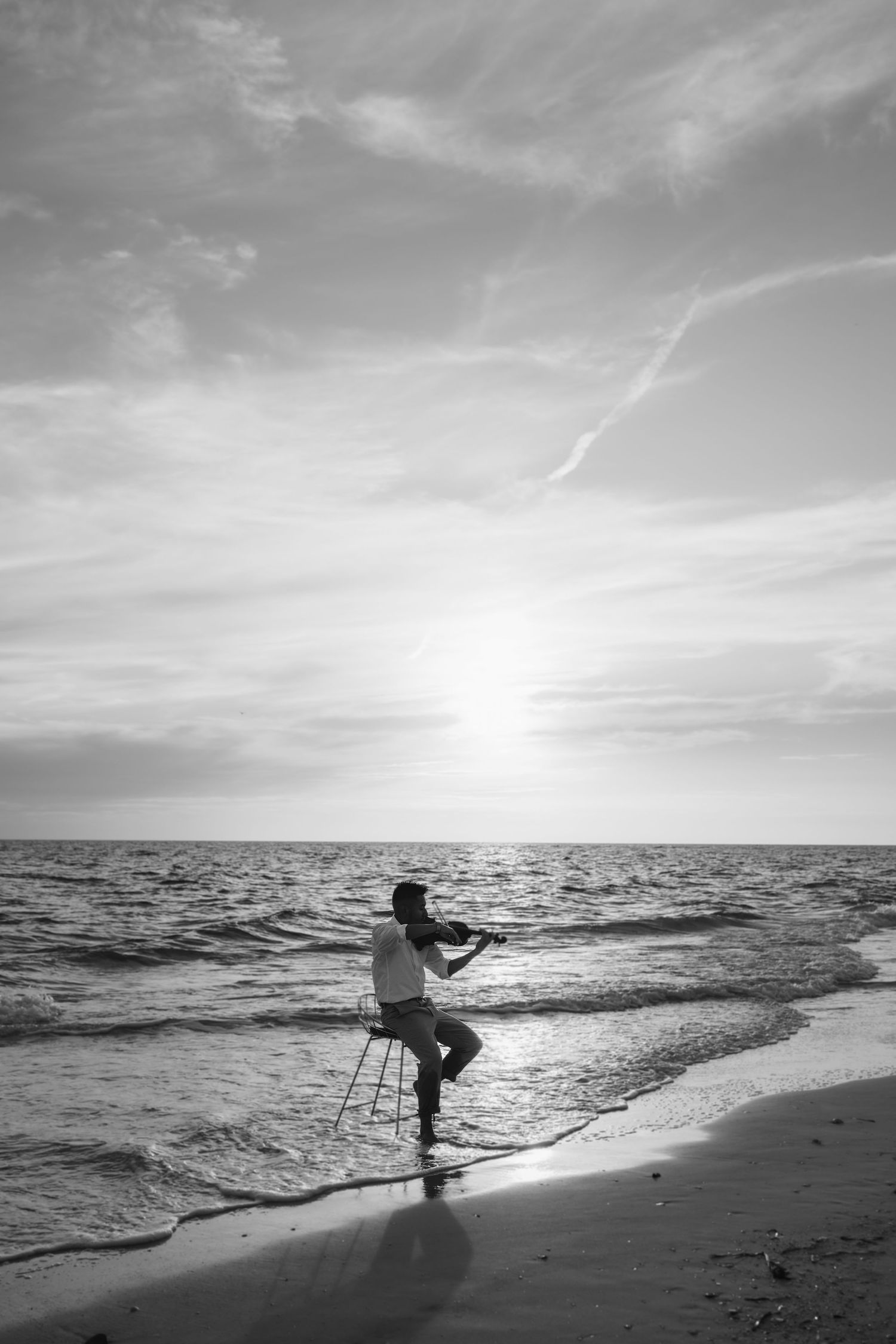 A silhouetted figure stands on a beach at sunset casting a long shadow across the sand and waves.