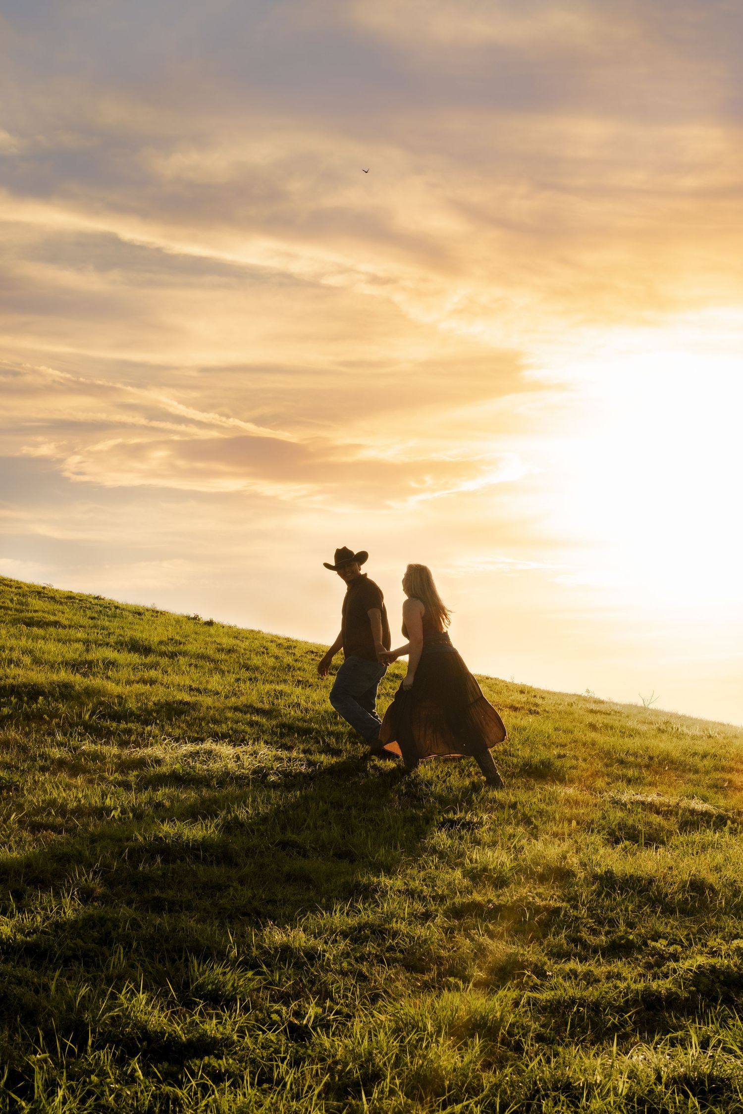 Silhouette of couple holding hands on grassy hill during vibrant golden sunset.