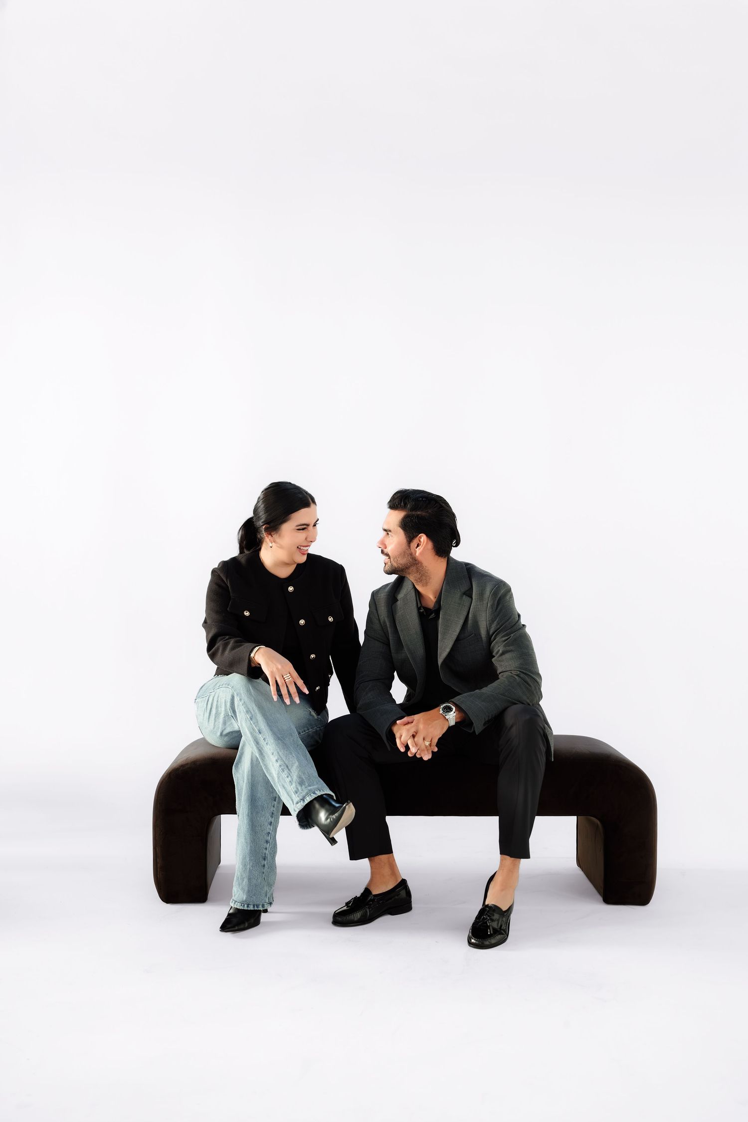 Two people sit and converse casually on a white background in a minimalist artistic photo series.