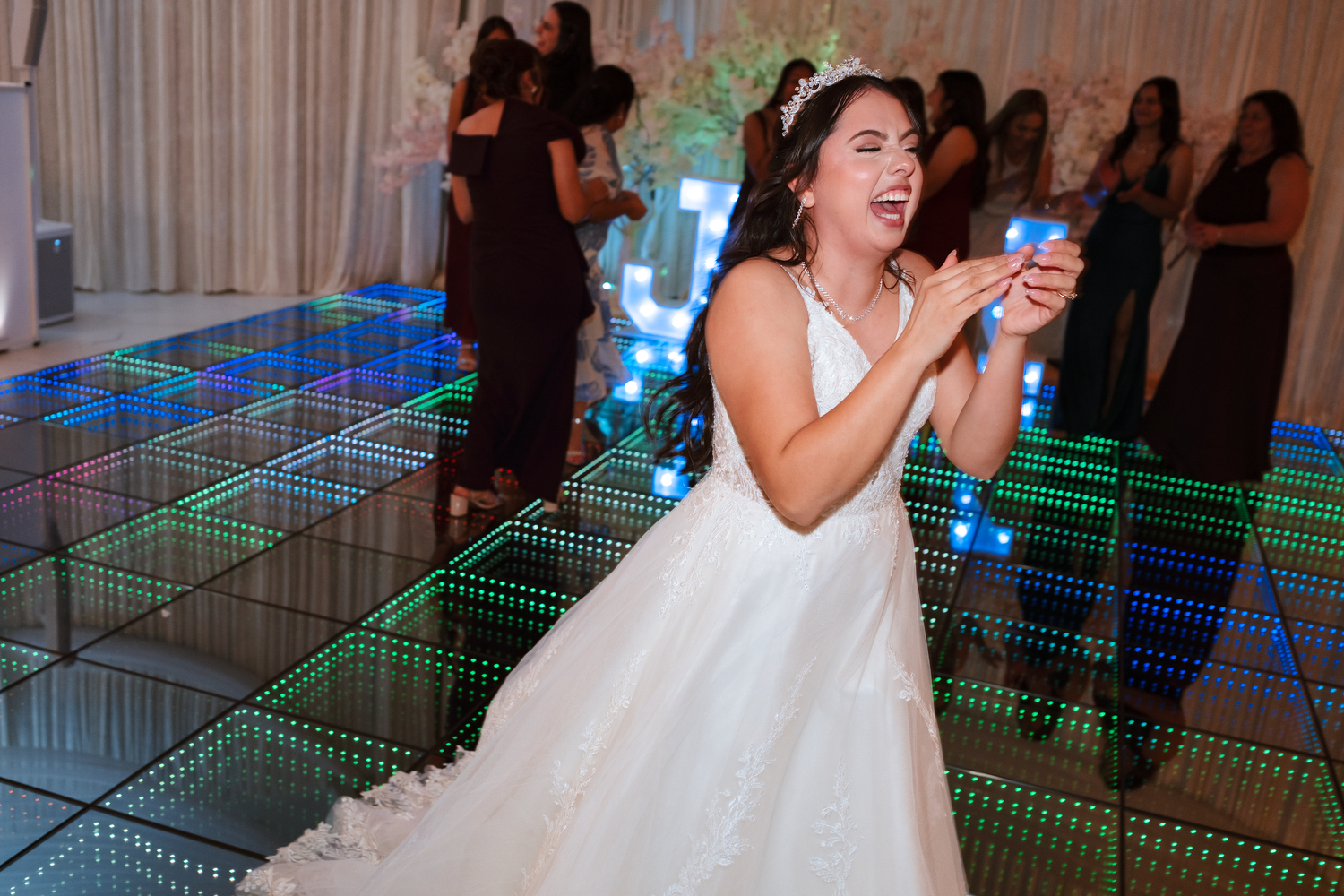 Bride in white gown dancing joyfully on illuminated LED dance floor at wedding reception.
