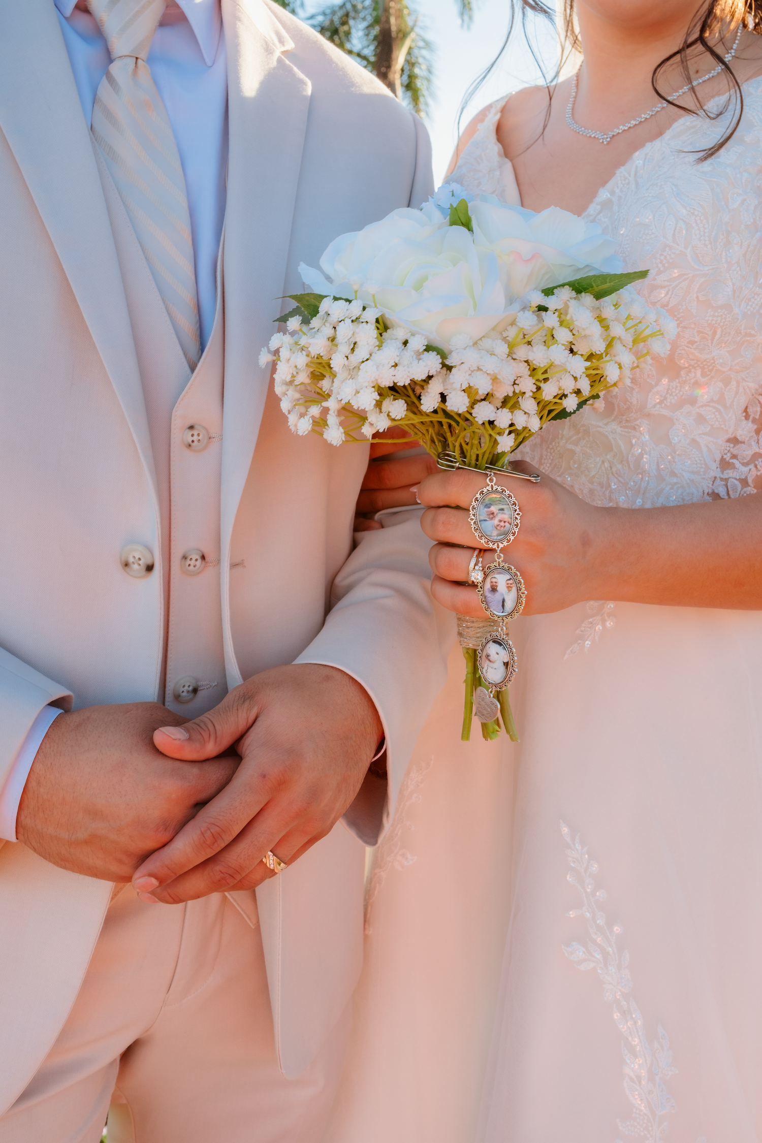 Close-up of bride and groom holding white bouquet with sentimental photo charm bracelet at wedding.