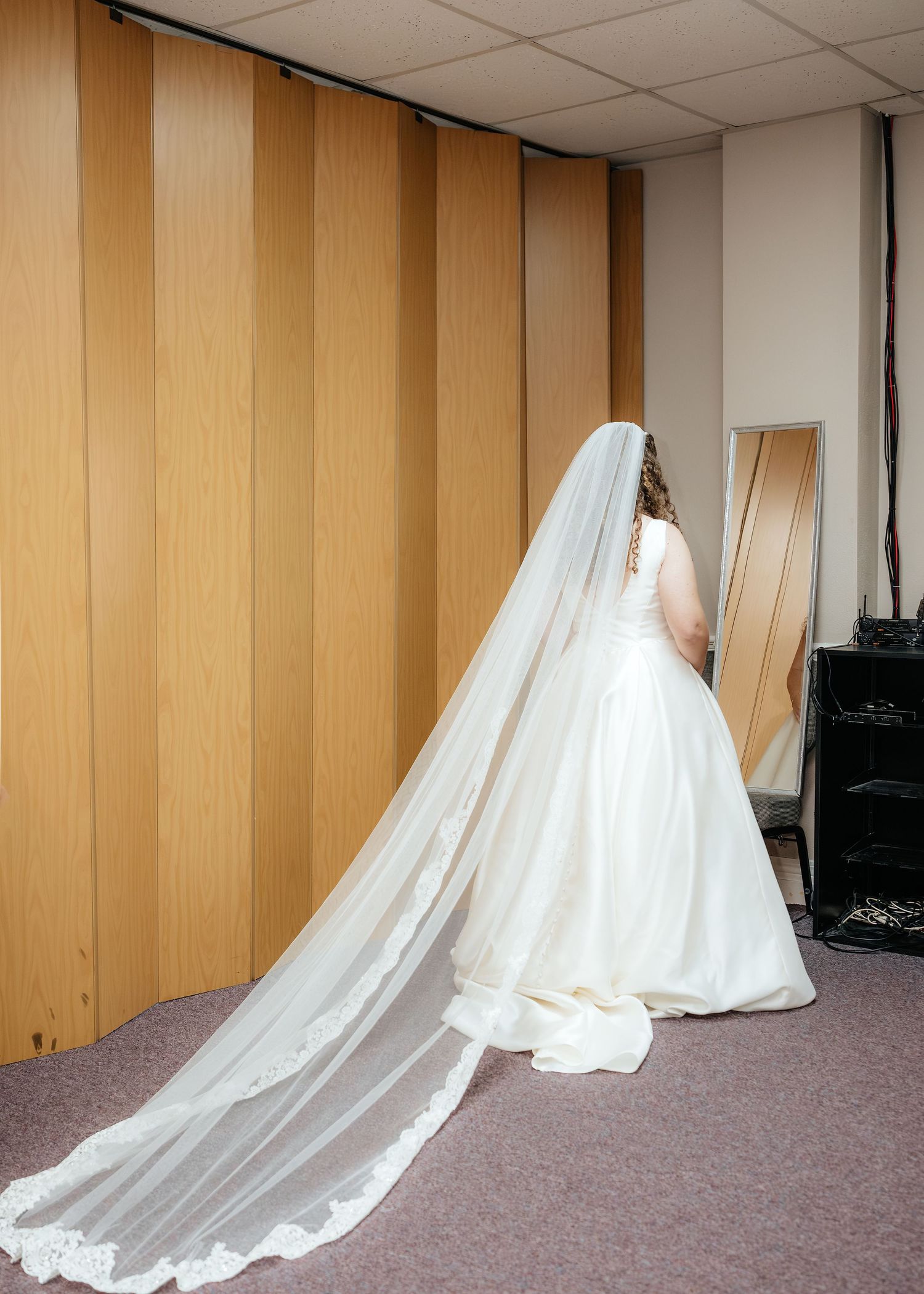 Bride in white ball gown with long lace-trimmed cathedral veil standing in a room before her wedding ceremony.