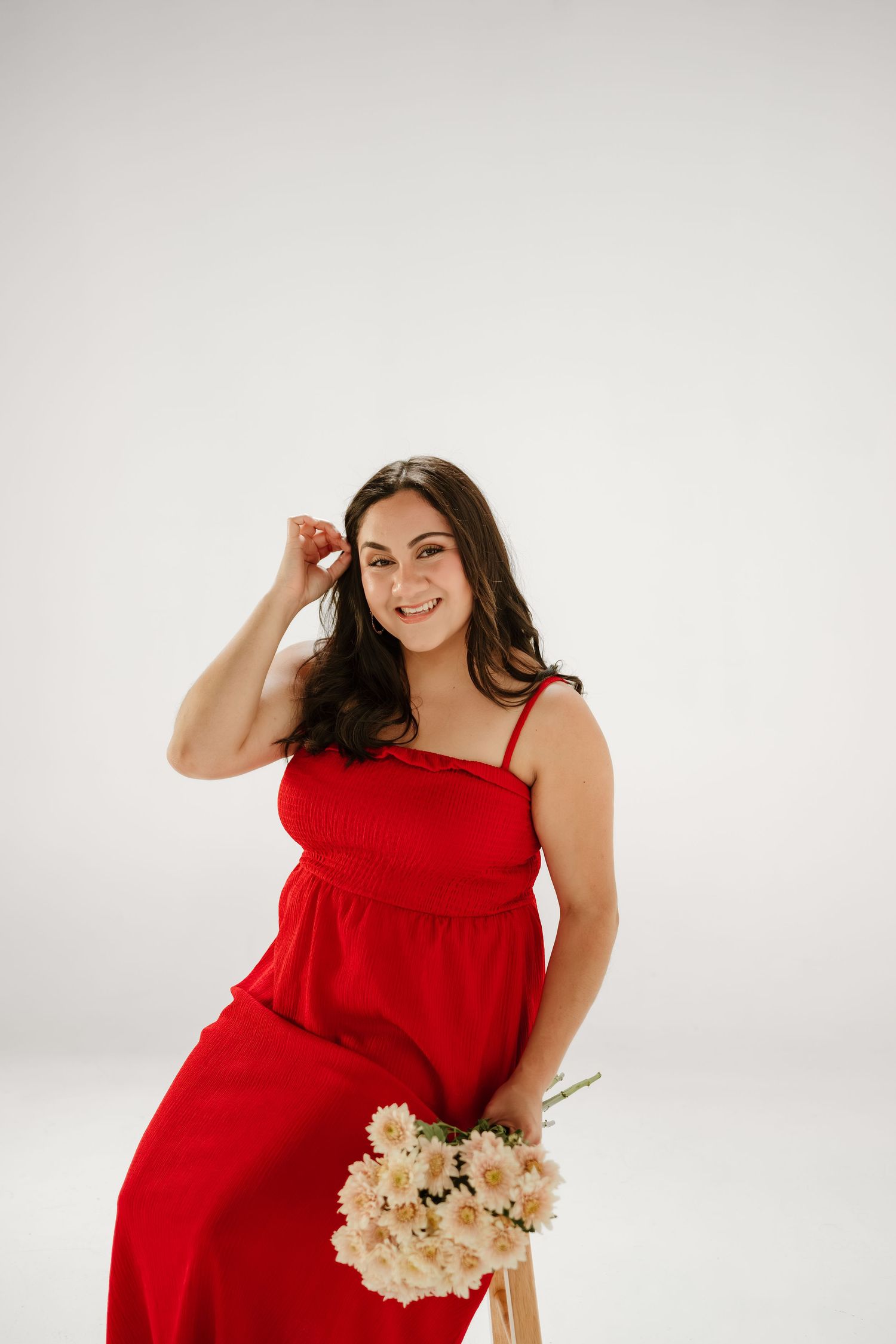 Woman in red dress holding white flowers, smiling while seated against a white background.