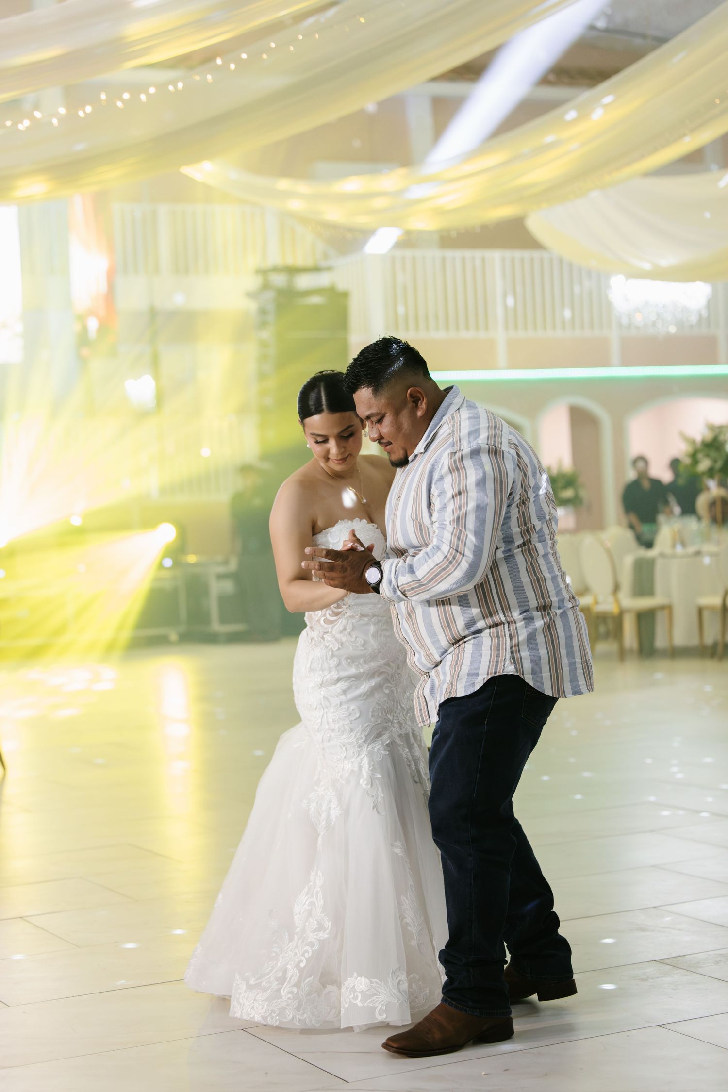 Bride and groom share an intimate first dance in a beautifully decorated wedding reception hall with draped white fabric.