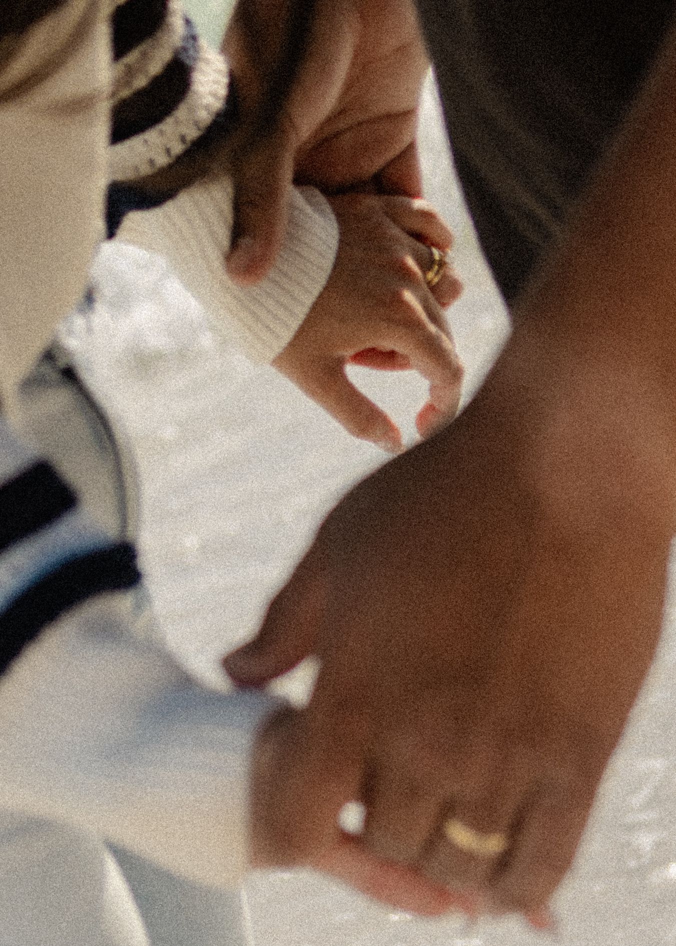 Close-up of two people holding hands, both wearing gold rings, one in a white knit sweater.