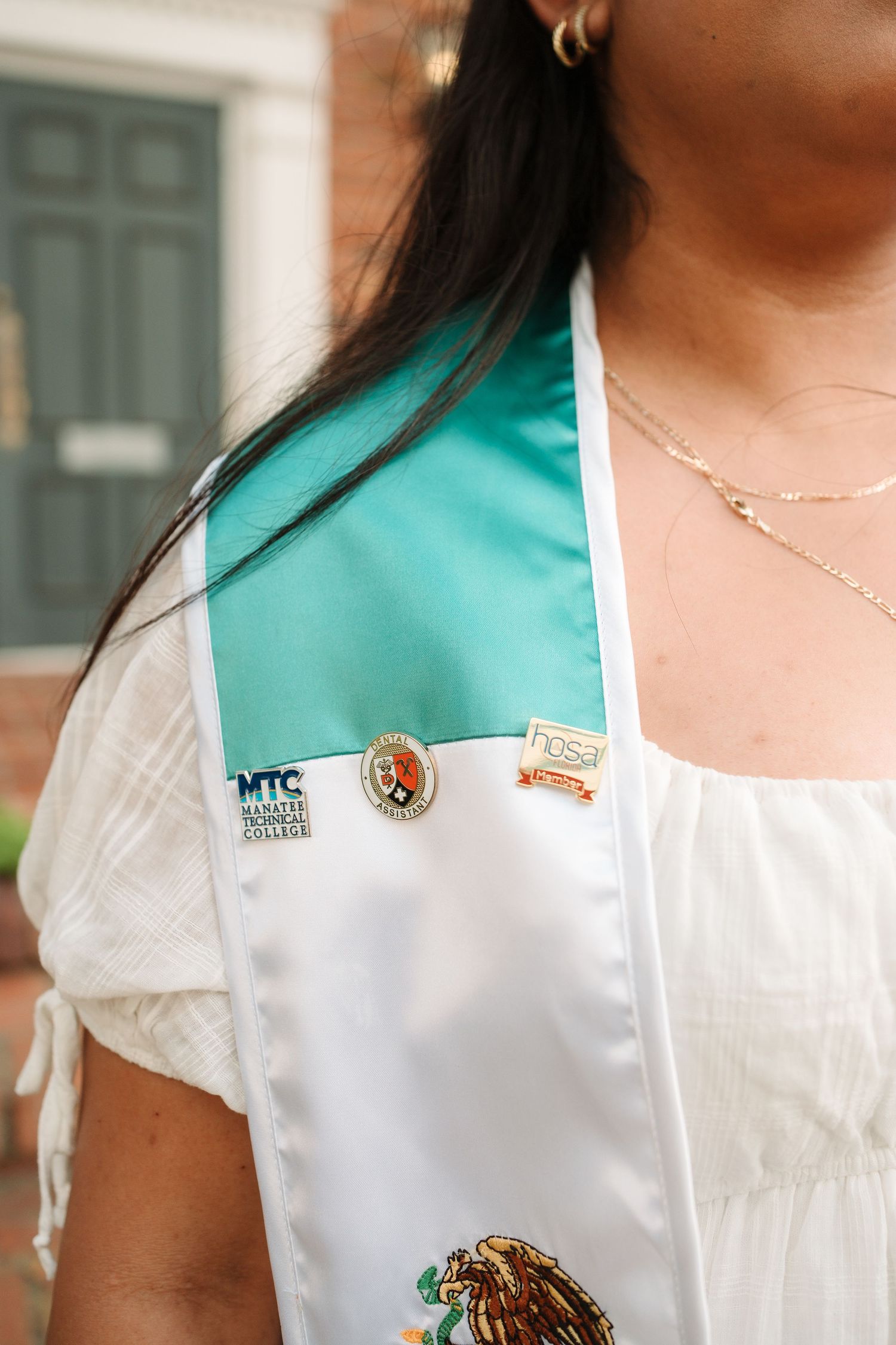 Graduate wearing a Mexican flag stole with MTC Manatee Technical College pin and HOSA pin at graduation.