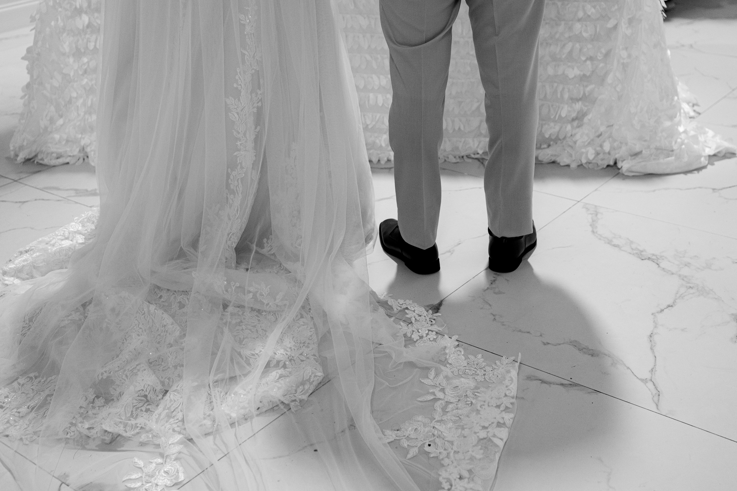Black and white photo of bride in lace wedding gown and groom in suit standing together on marble floor.