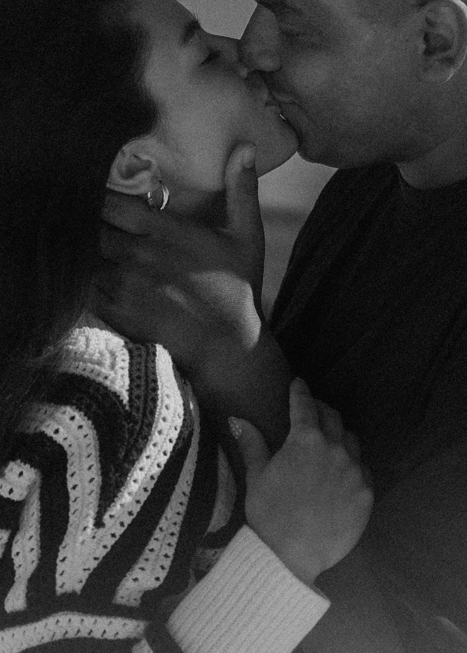 Black and white photo of a couple sharing a romantic kiss, woman wearing striped sweater and hoop earring.
