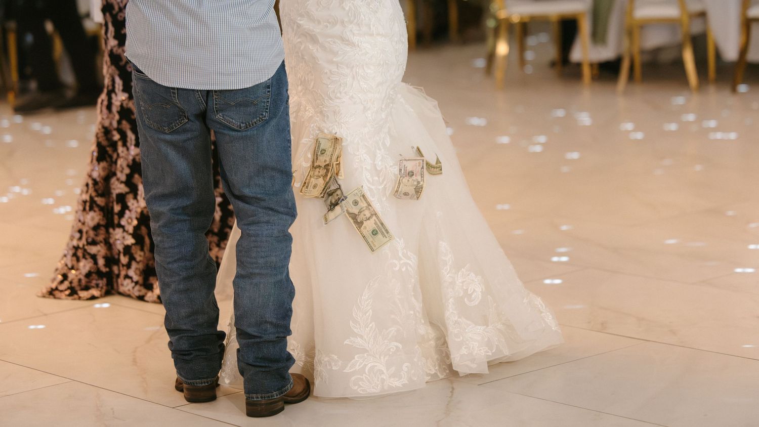 A bride and groom share a first dance with dollar bills pinned to the wedding dress.