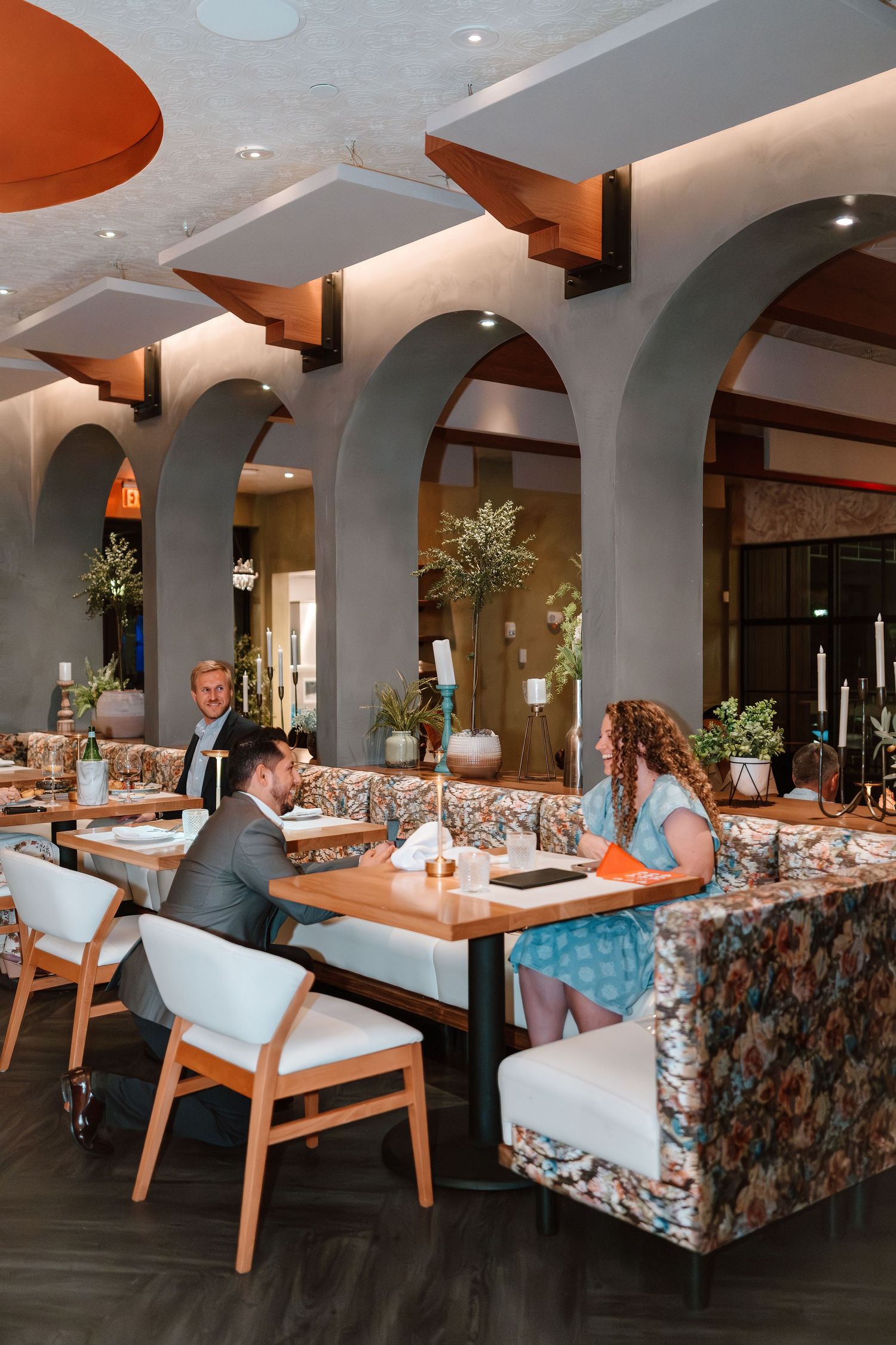 Elegant restaurant interior with arched walls, floral booths, and diners enjoying a meal in a sophisticated setting.