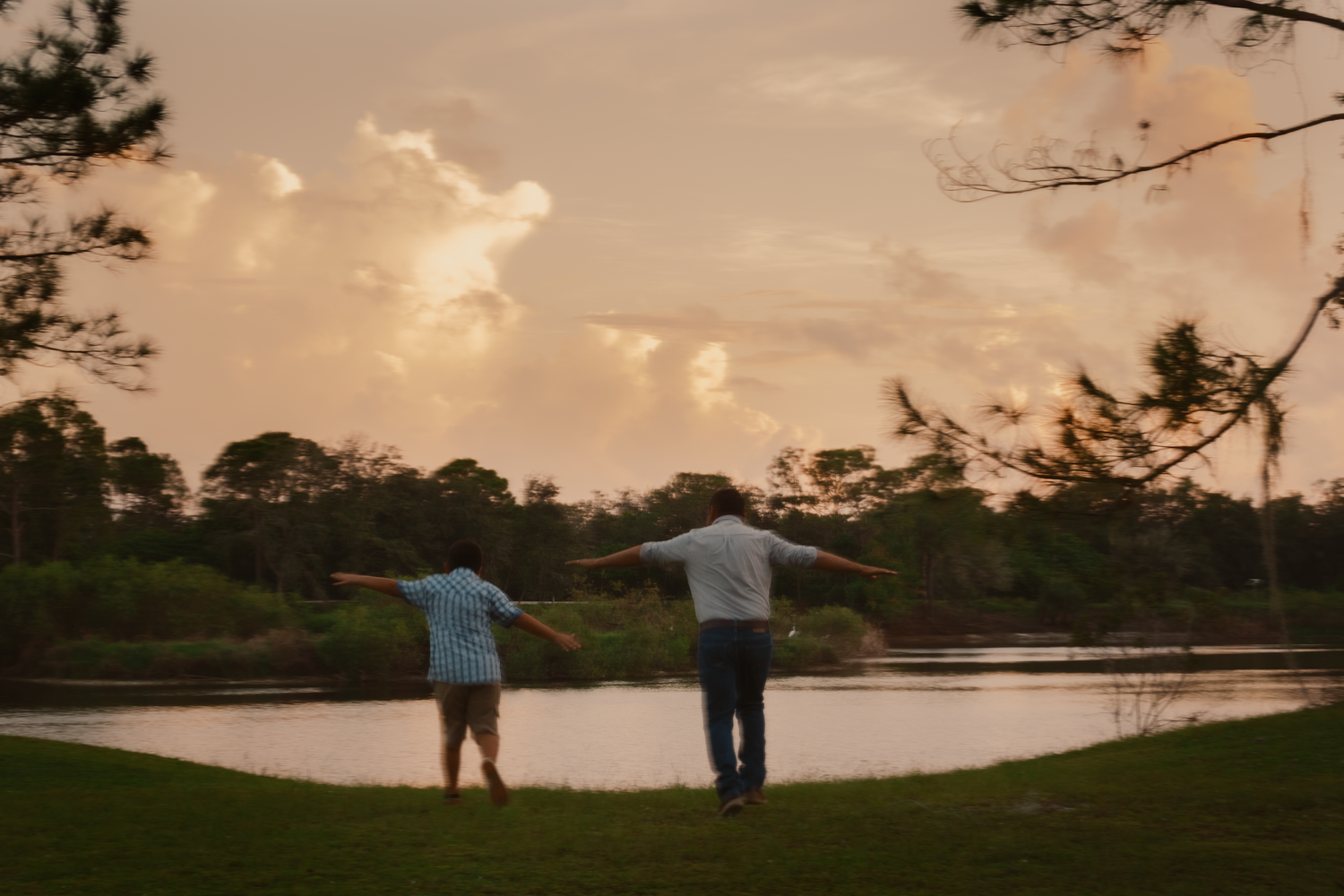 Two people standing by lake at sunset with dramatic clouds.