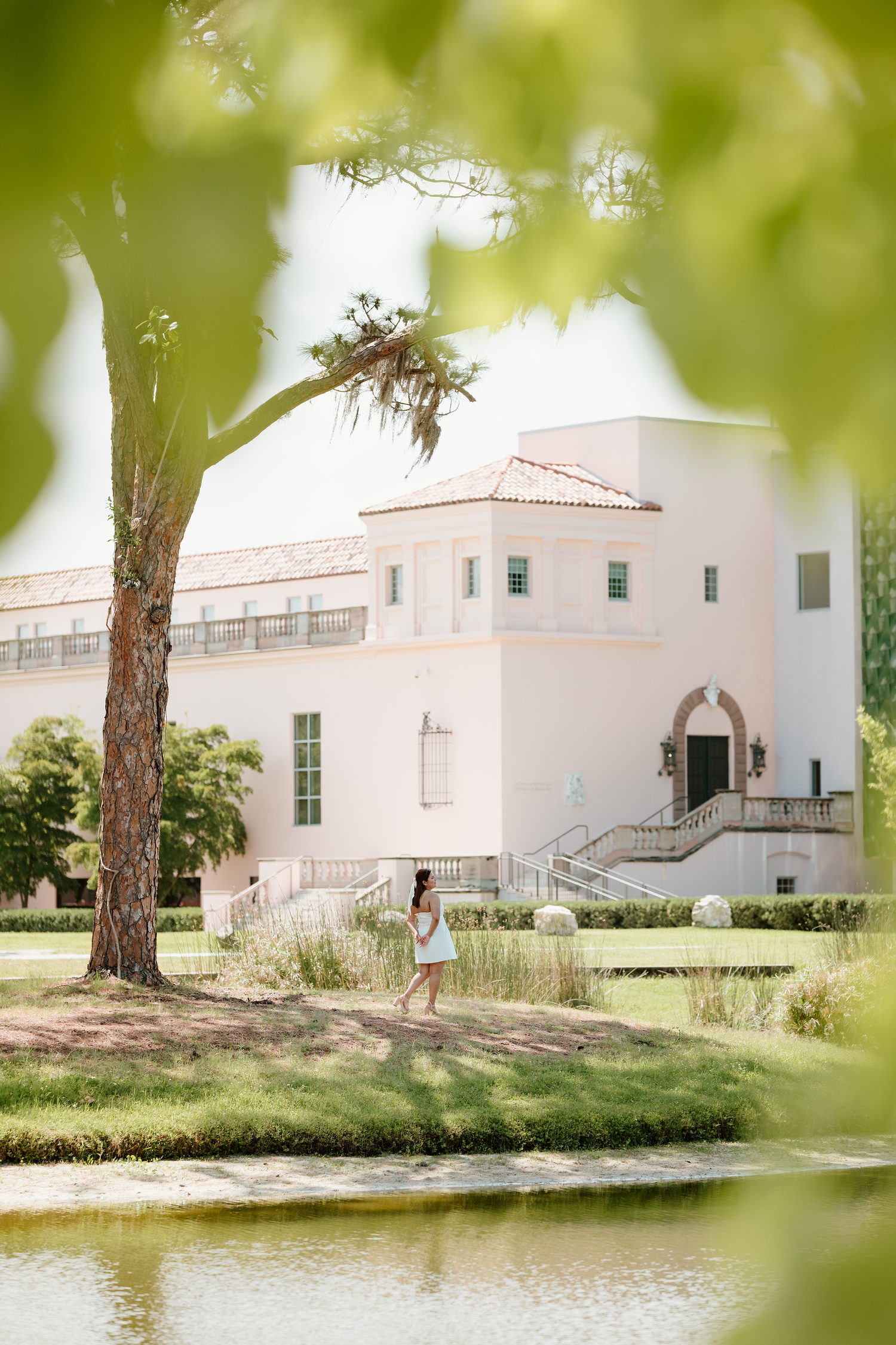White Mediterranean-style building with arched entrance reflected in pond with lush greenery.