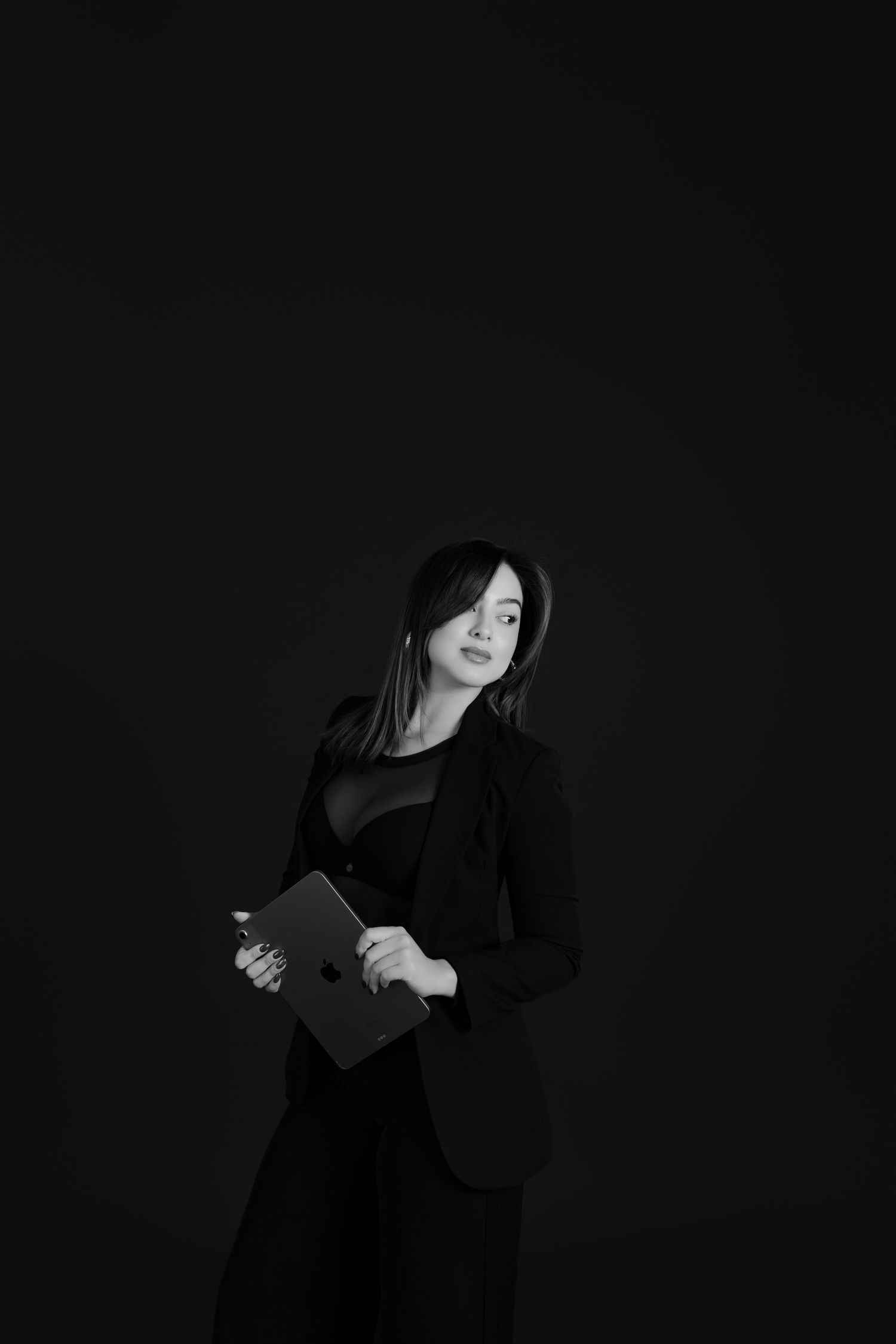 Professional woman in black blazer holding tablet in dramatic black and white studio photo.