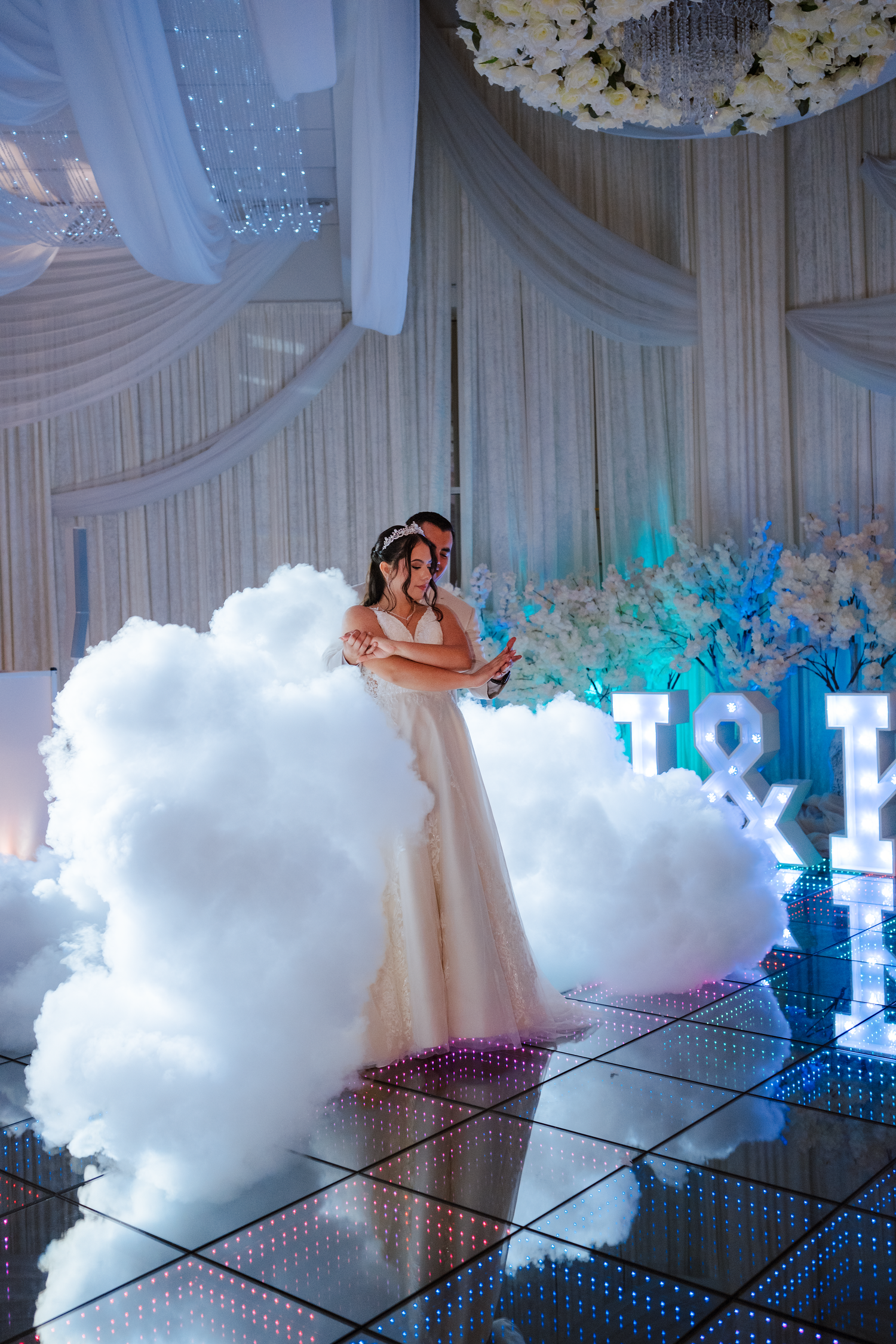 Bride and groom sharing first dance surrounded by dramatic fog on mirrored dance floor at reception.