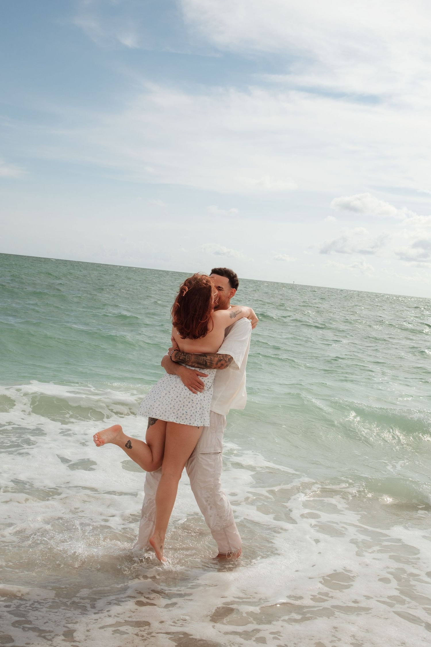 A romantic couple embraces in the shallow ocean waves at the beach during a sunny day.