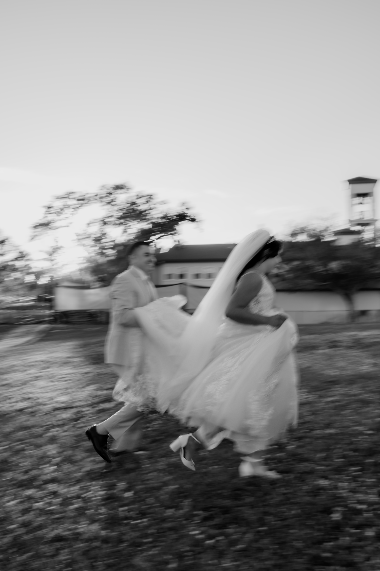 Black and white photo of bride and groom running outdoors on their wedding day with motion blur effect.