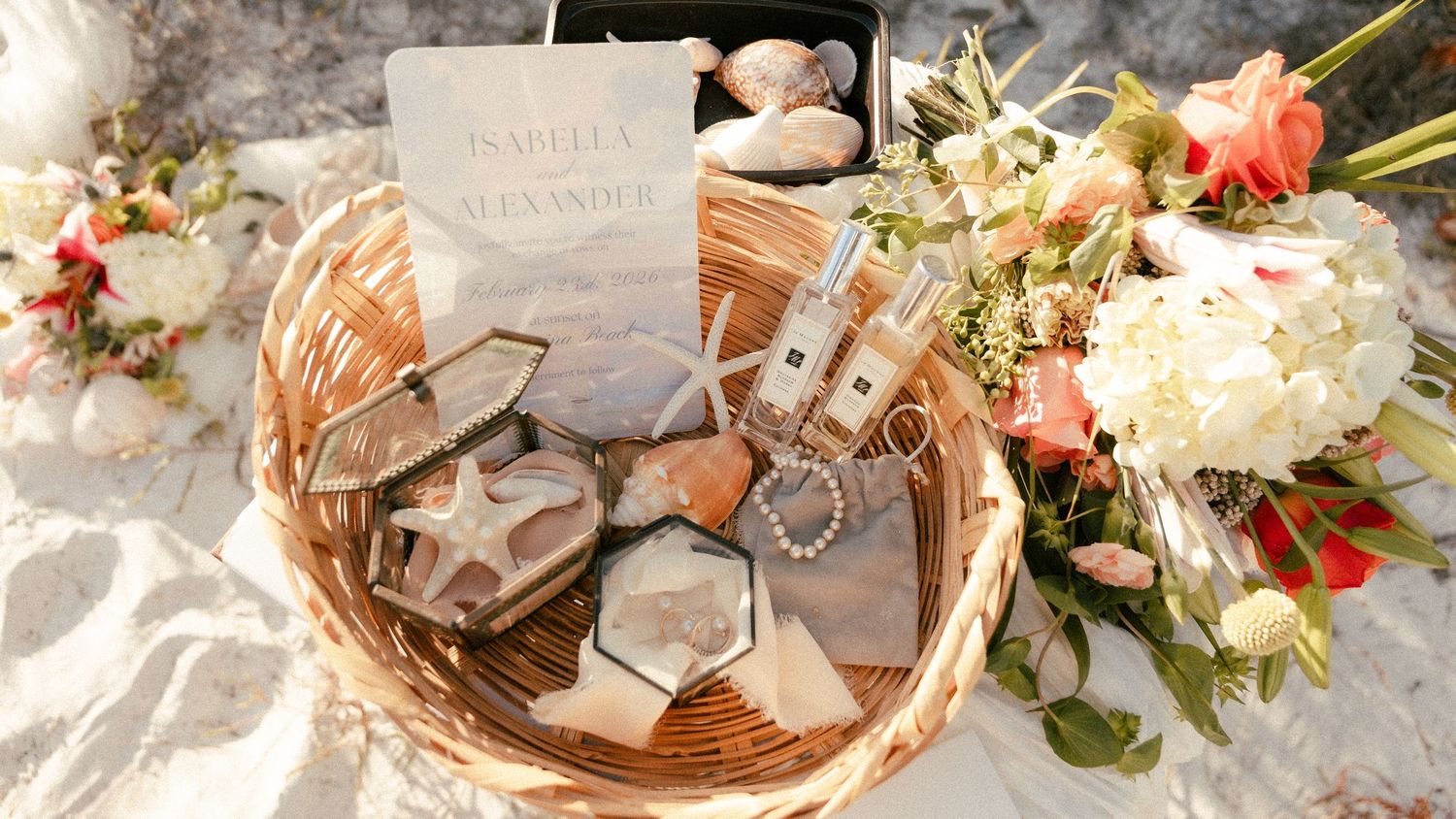 A wicker basket with wedding stationery, geode crystals, Jo Malone perfume, pearls, and floral arrangements.