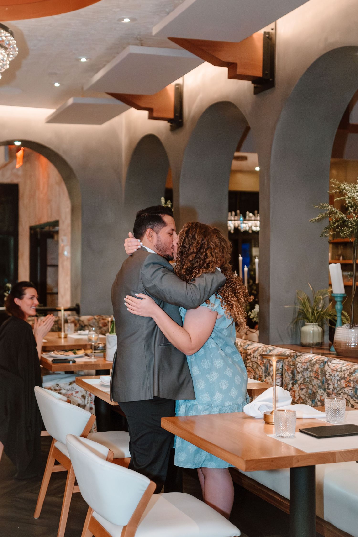 Couple sharing a romantic kiss in an elegant restaurant with arched walls and modern decor.