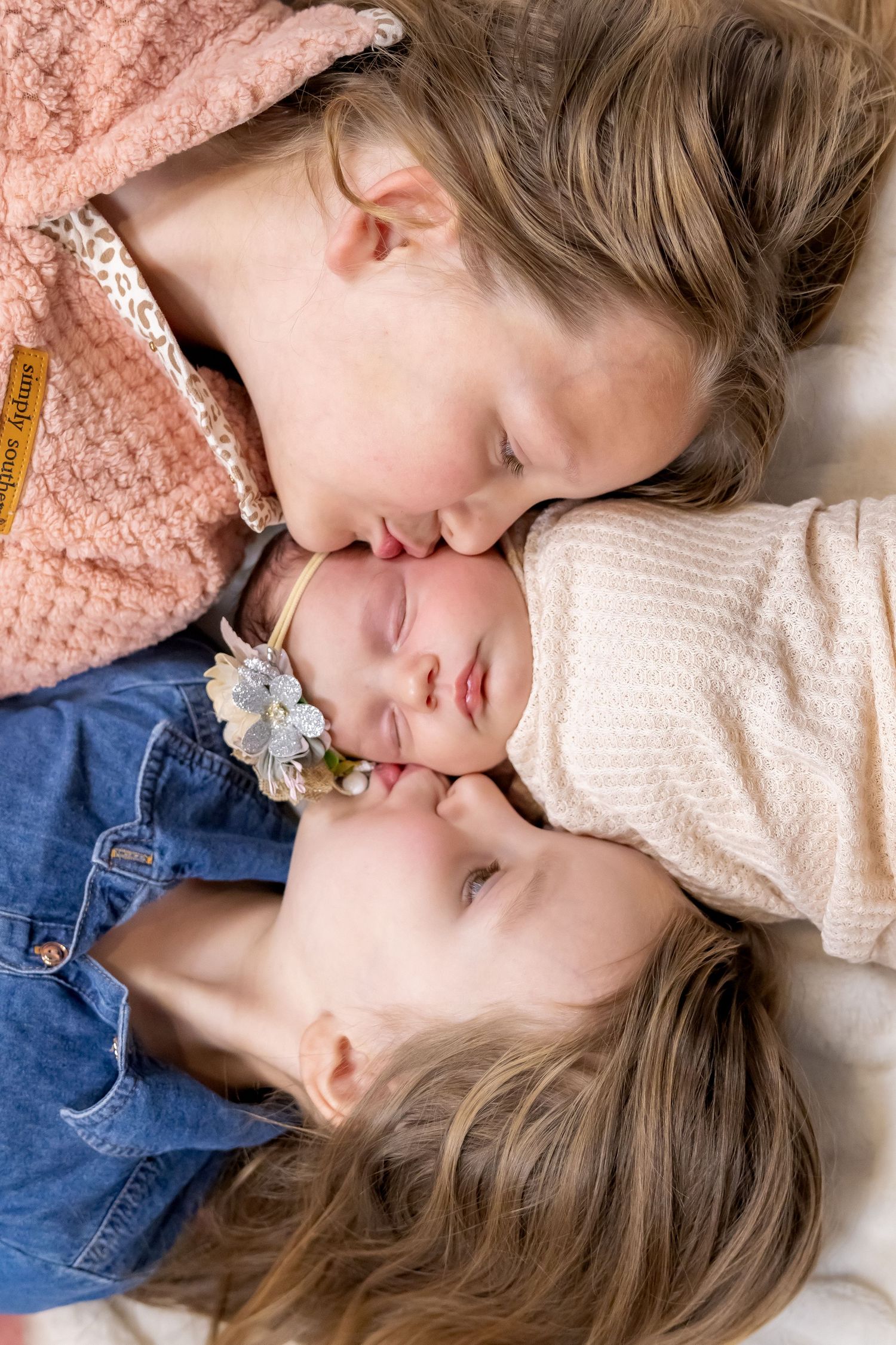 Three siblings share tender moment lying close together during portrait session.