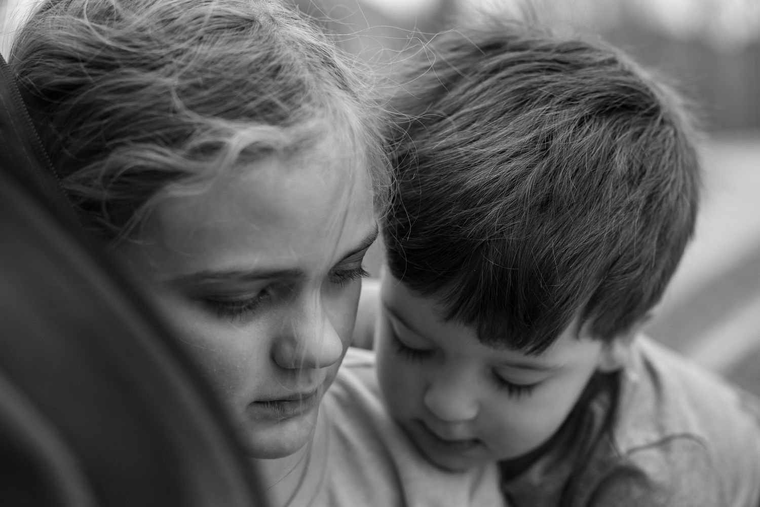A black and white image shows a tender moment between two people in close proximity with soft lighting.