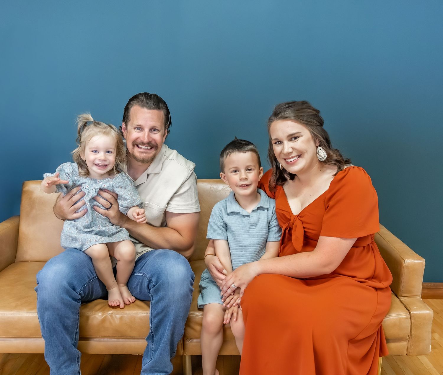Relaxed family photo session on leather couch with blue wall backdrop.
