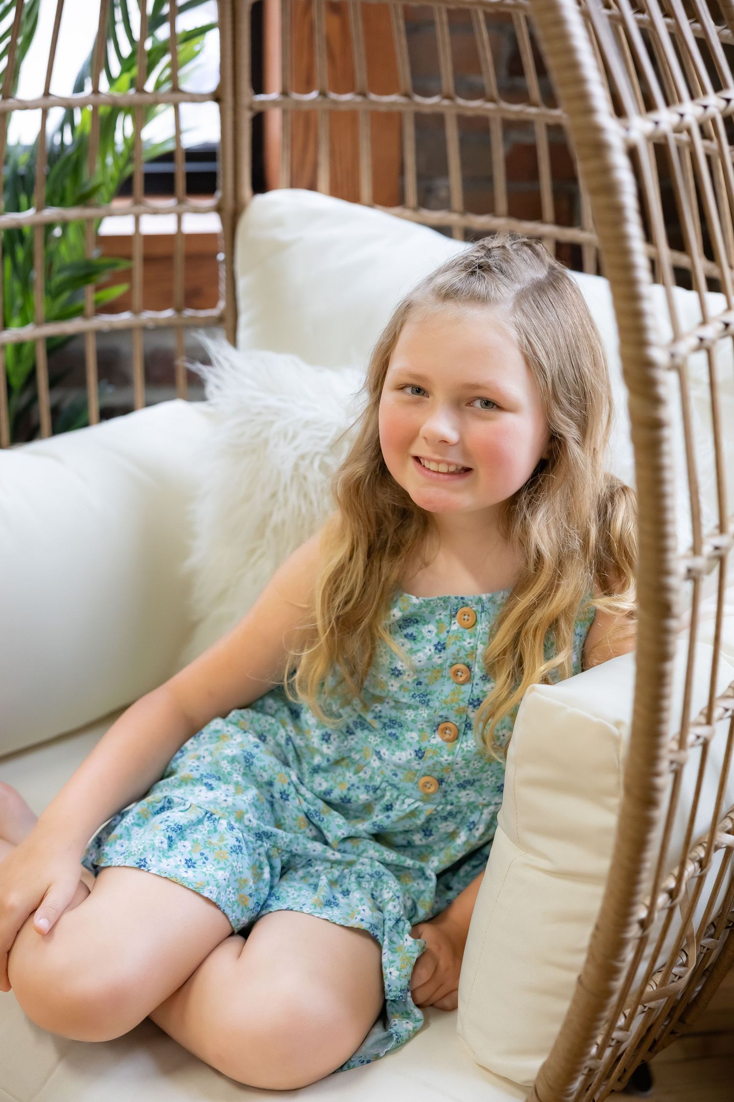 Child relaxes in woven hanging chair wearing floral summer dress.