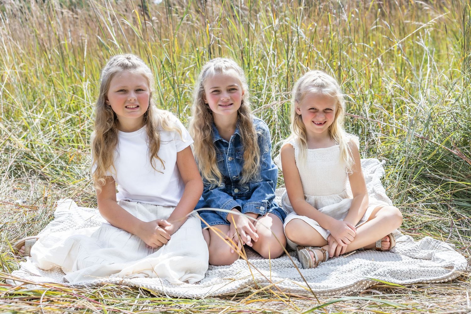 Children sitting together on a blanket in a field of tall grass during golden hour.