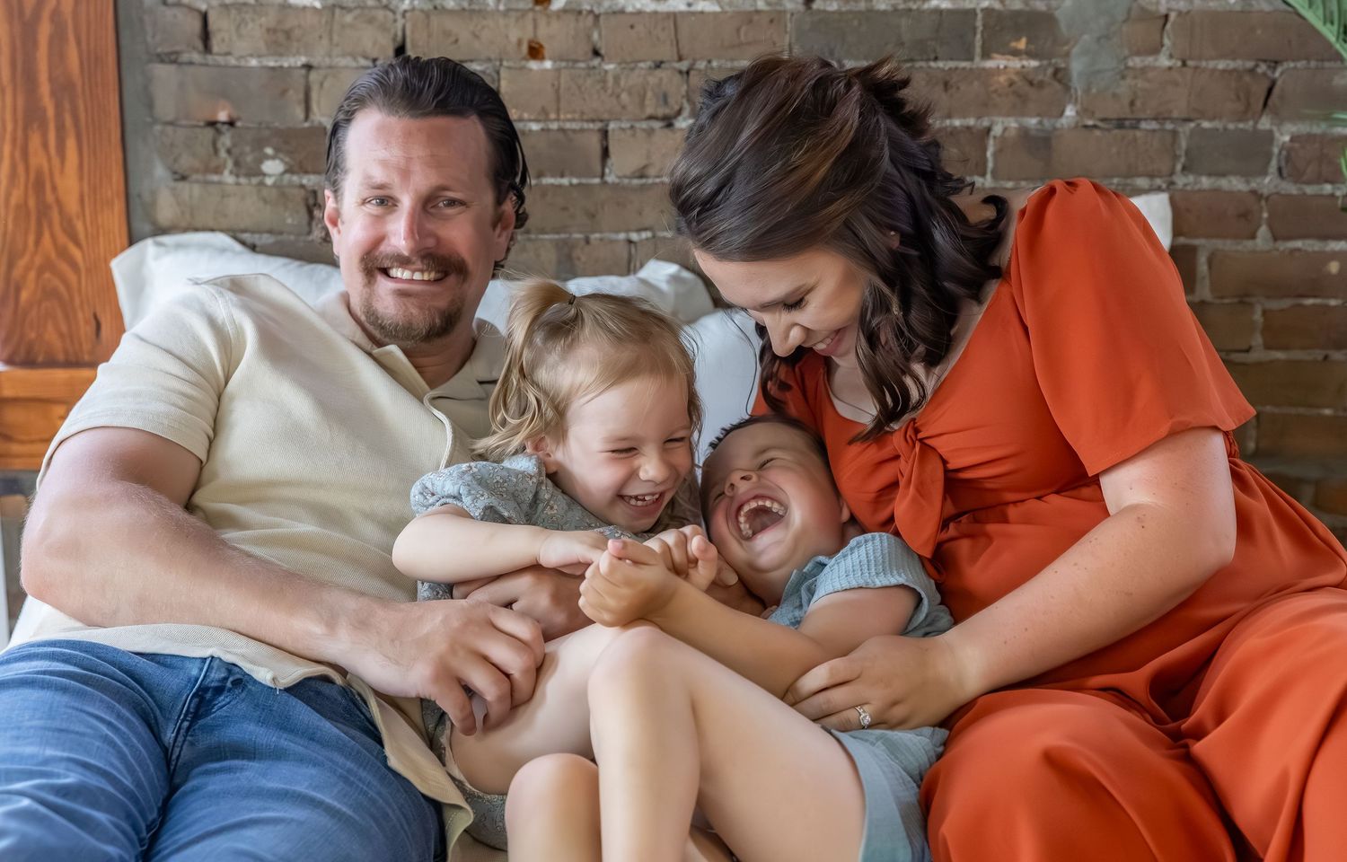 Candid family laughter captured on couch with brick wall background.