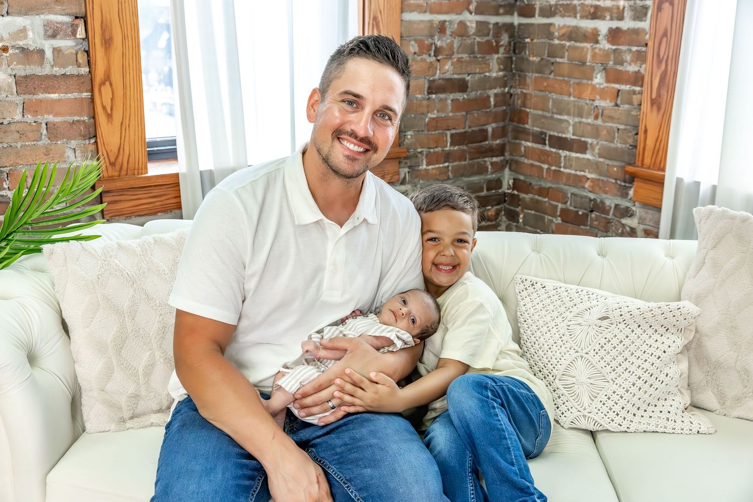 A family enjoys quality time together on a white sofa in a room with brick walls.