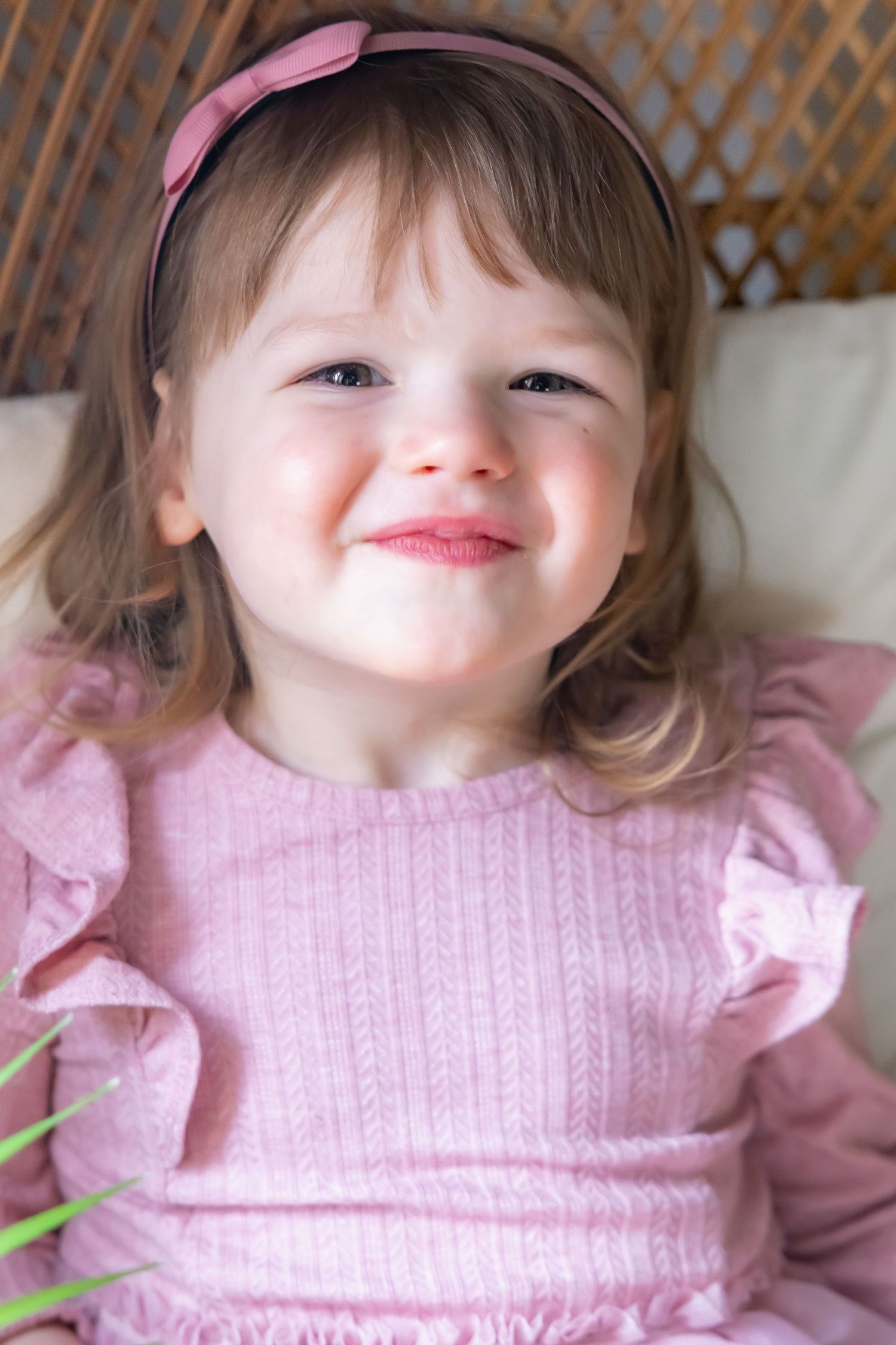 Child wearing pink knit sweater with ruffled sleeves smiling at camera.