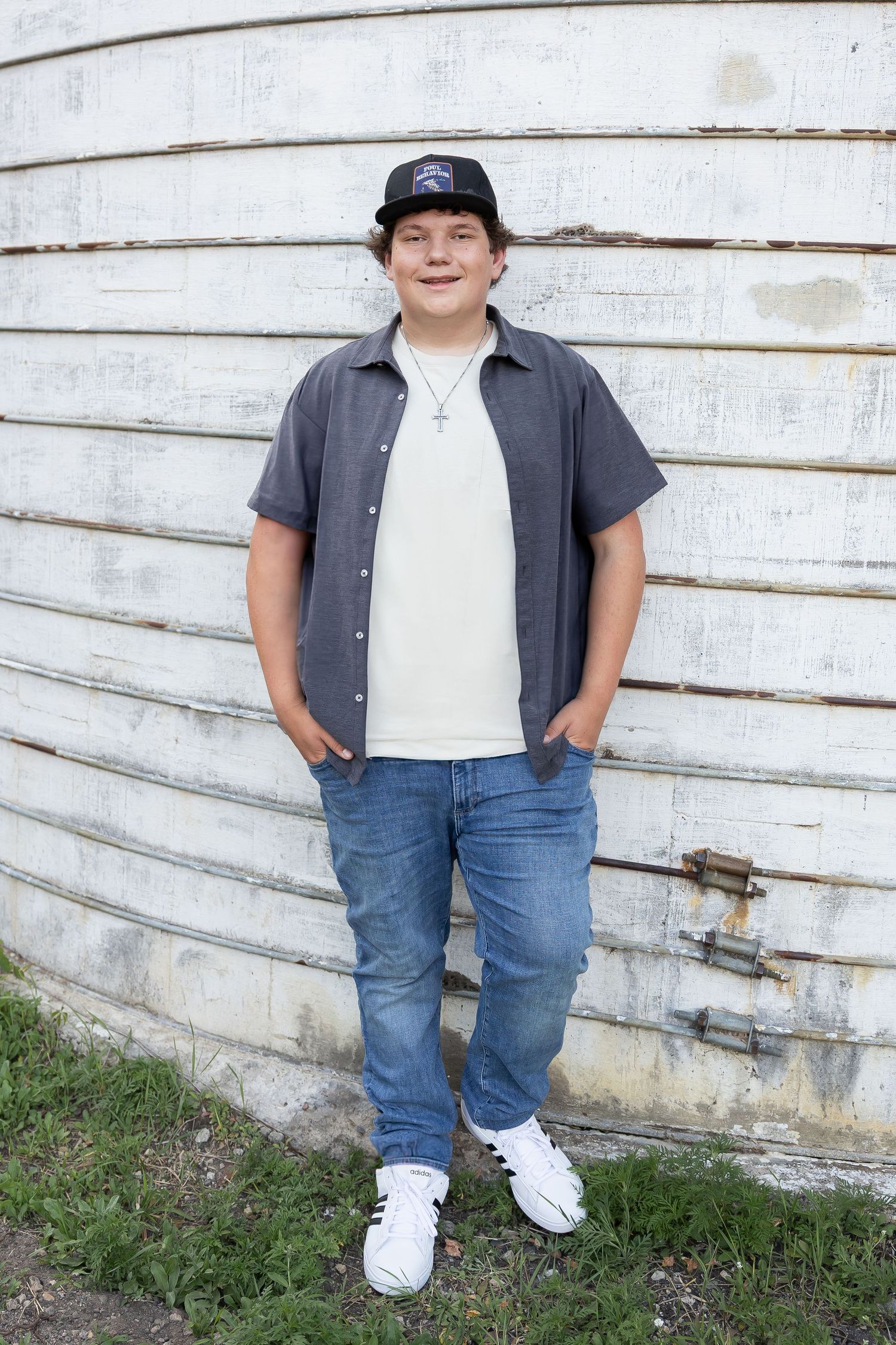 Casual pose against white wooden wall wearing baseball cap and button-down shirt.